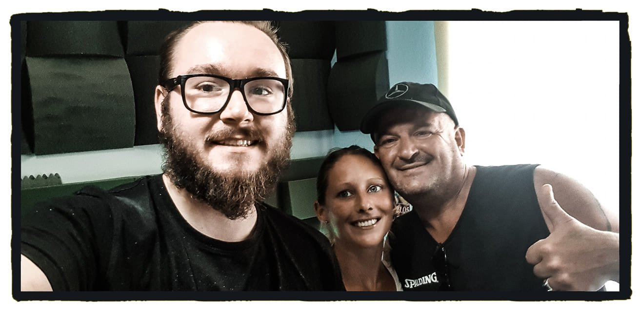 Three people taking a selfie indoors, smiling at the camera, with black acoustic foam panels in the background.