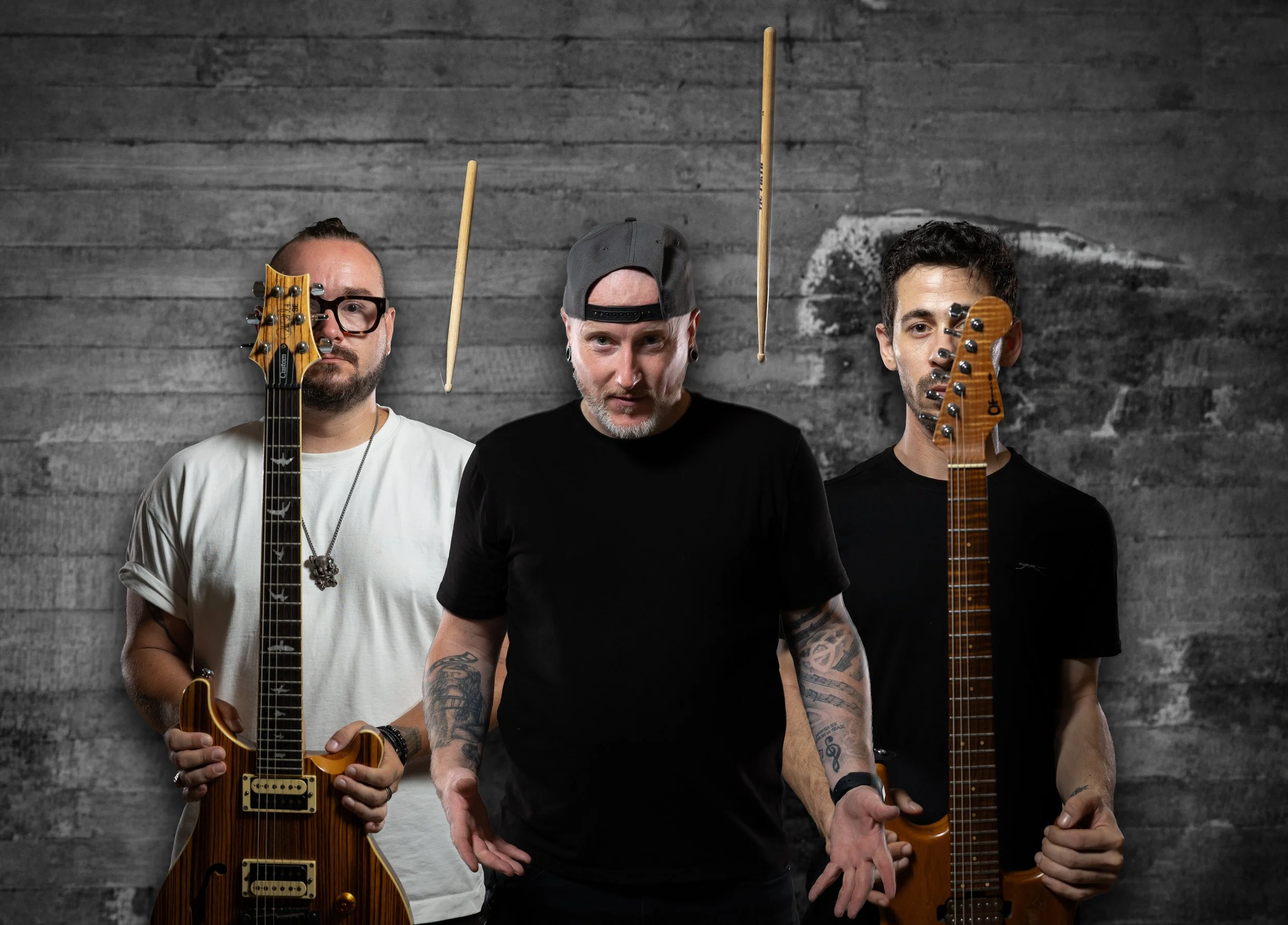 Three men standing against a dark wooden wall, each holding a guitar and facing the camera.