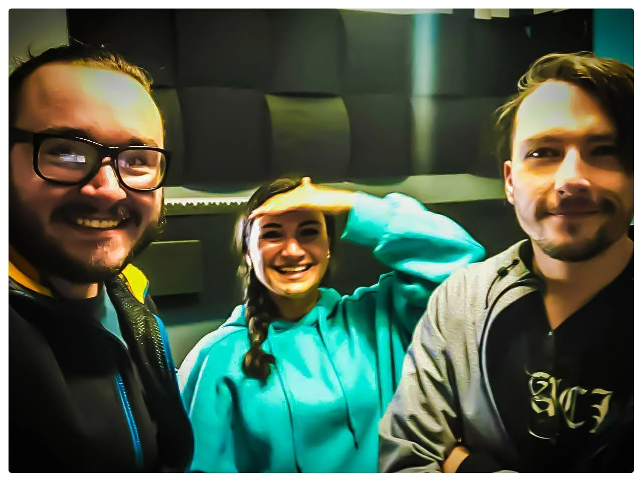 Three young people smiling and taking a selfie in a recording studio or soundproof room.