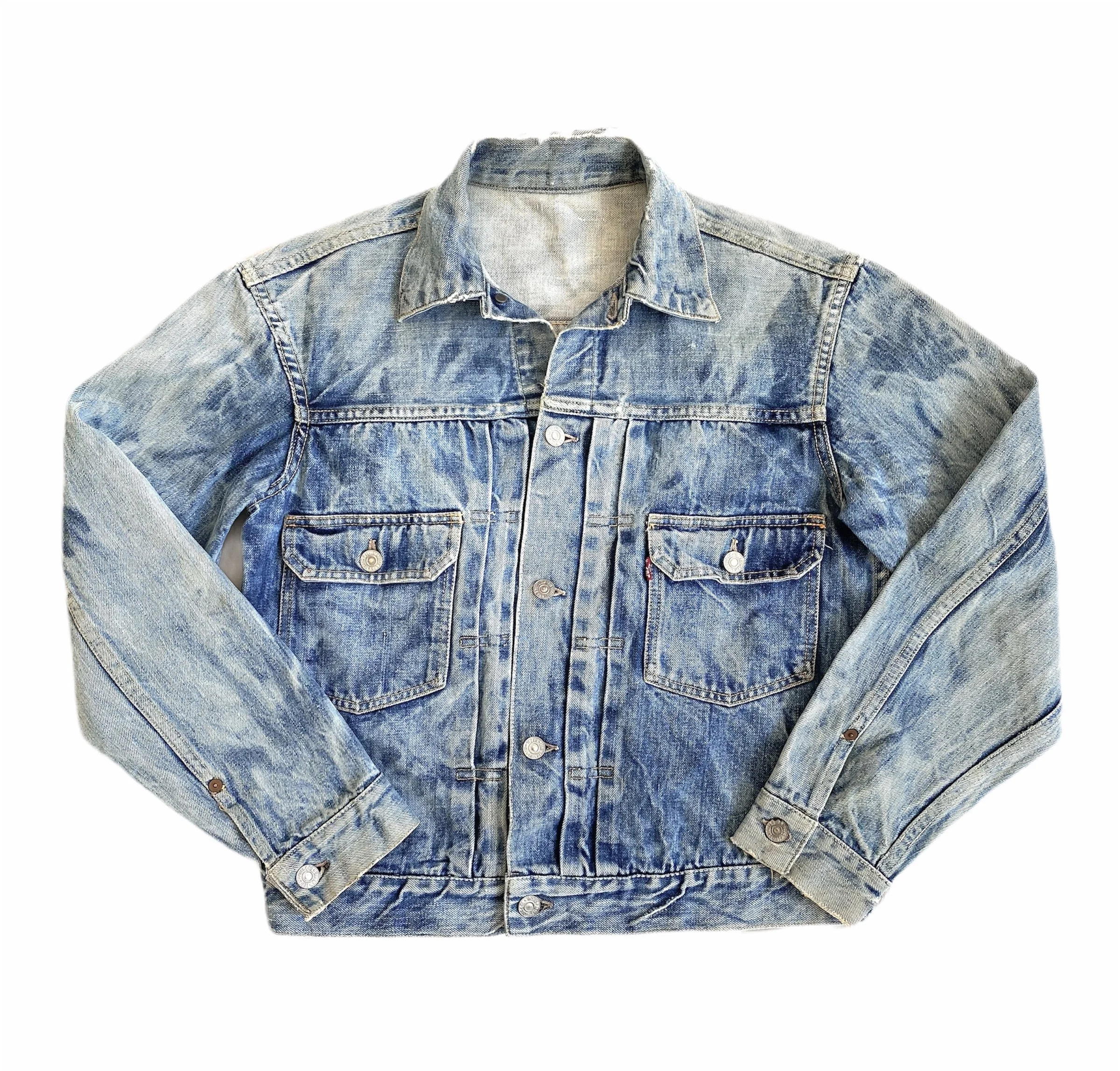 Close-up of a classic blue denim jacket with visible stitching and metal buttons, displayed against a white background.