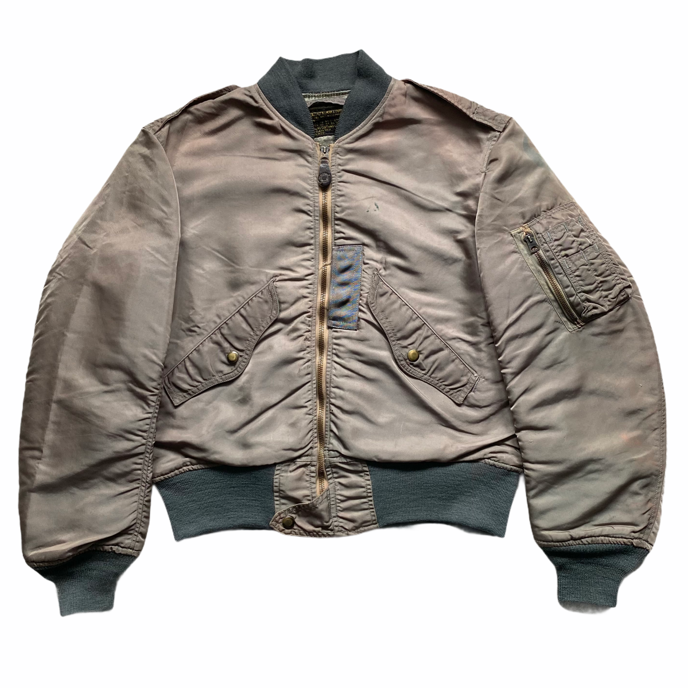 A men's bomber jacket in beige with a black ribbed collar, cuffs, and waistband, featuring a front zipper closure, multiple pockets, and shoulder epaulets.