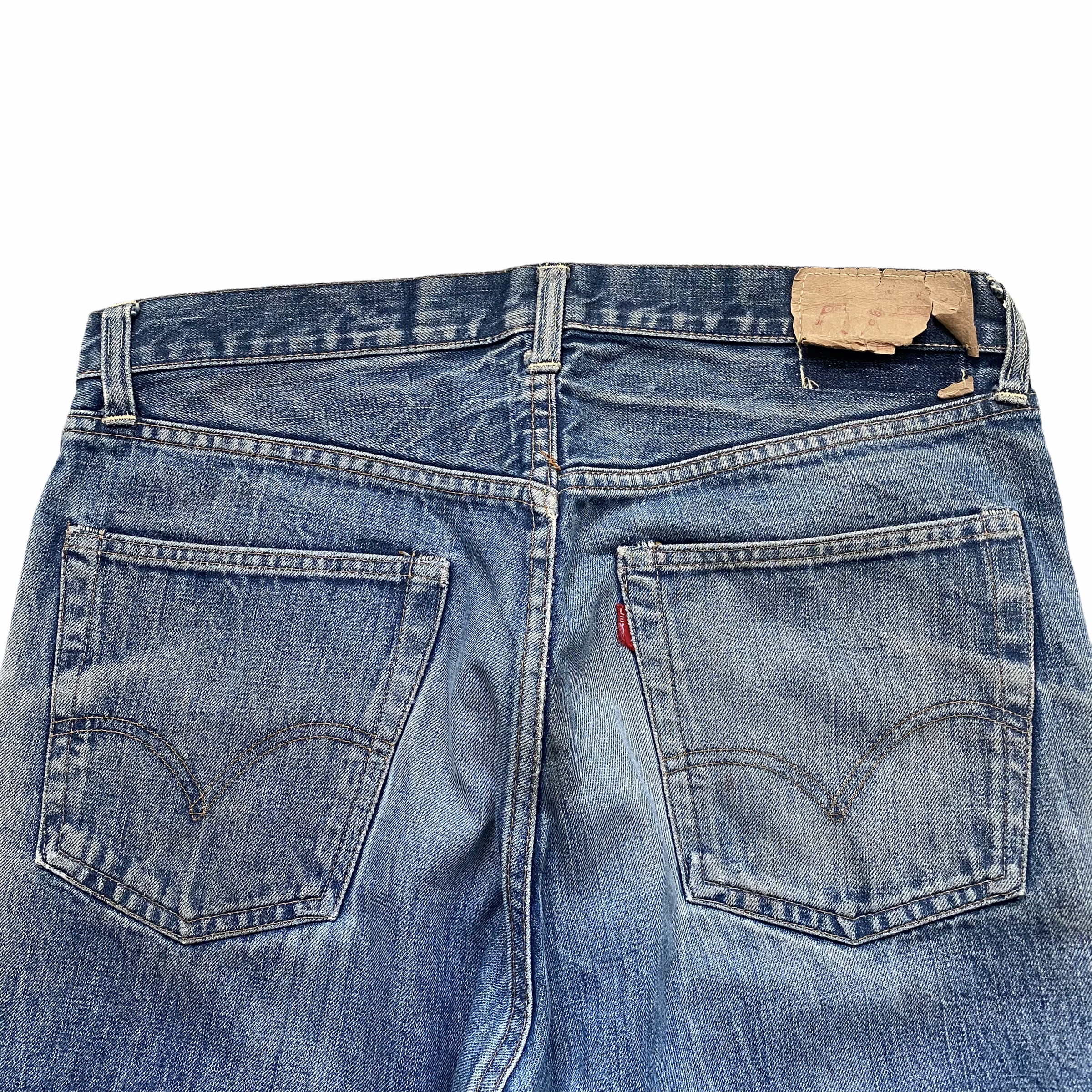 Close-up of the upper part of a pair of blue denim jeans, showing the waistband, belt loops, and a brown leather patch with a red tag.