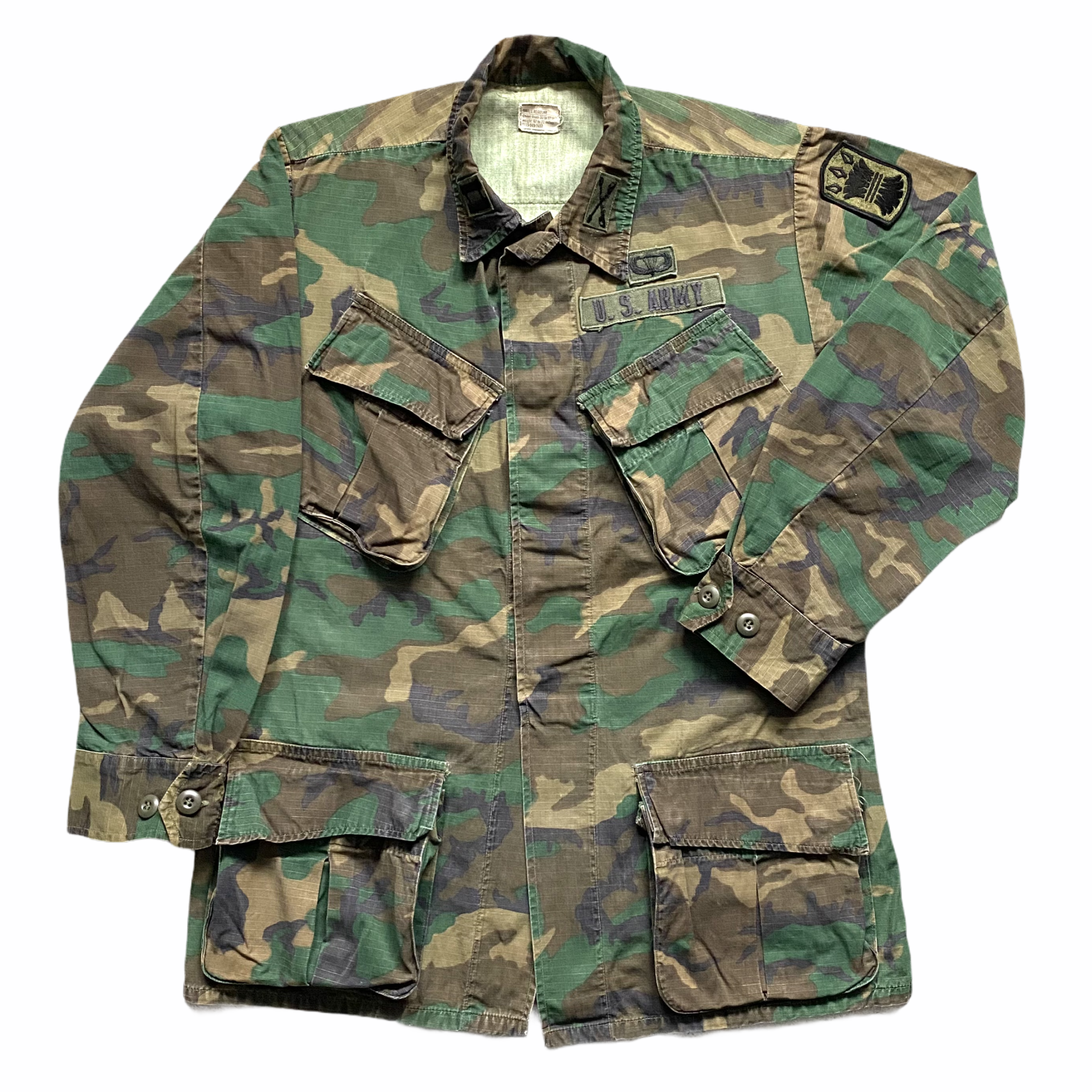 U.S. Army camouflage uniform jacket with patches and buttons, laid flat.