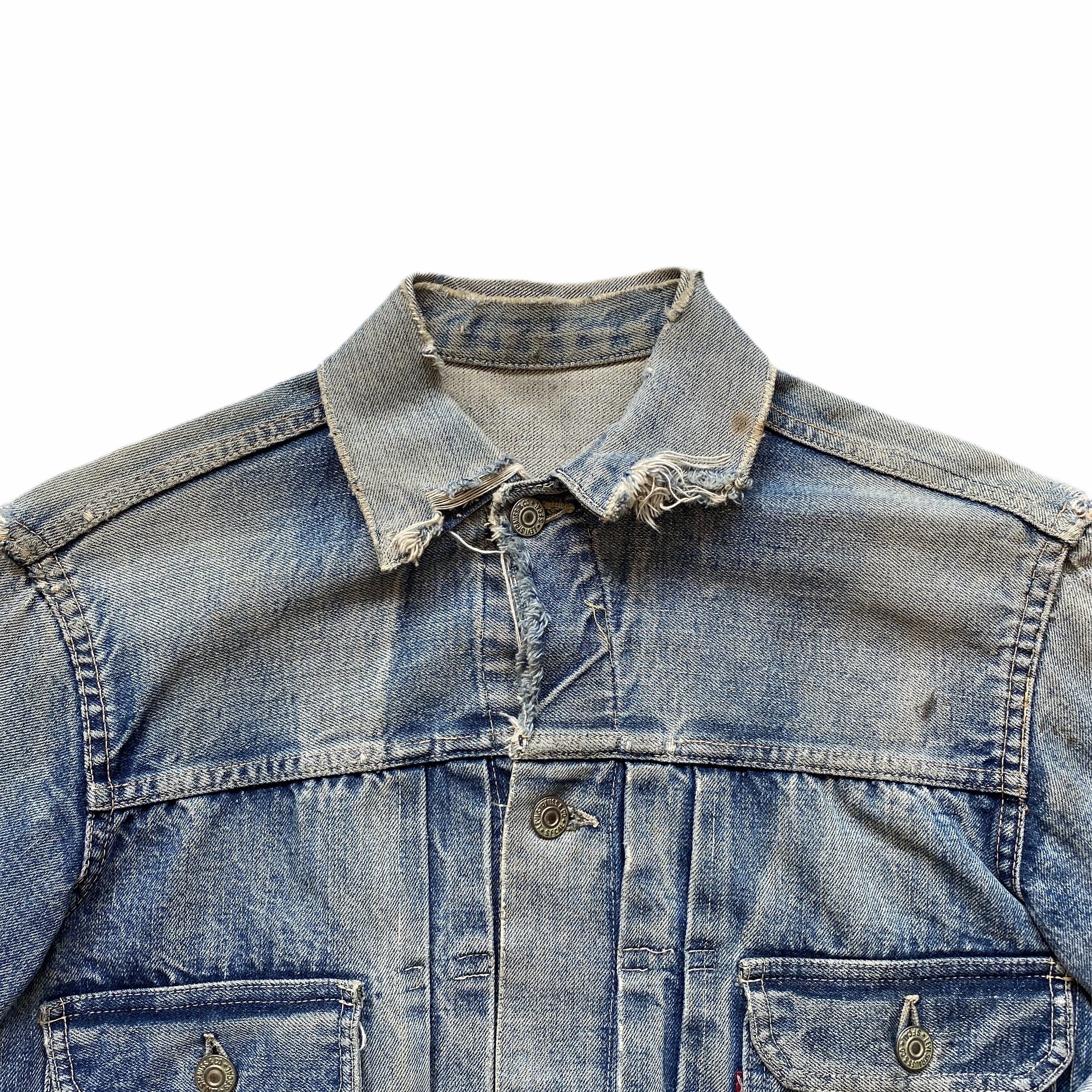 Close-up of a classic blue denim jacket with metal buttons and frayed collar, showing detailed stitching and fabric texture.