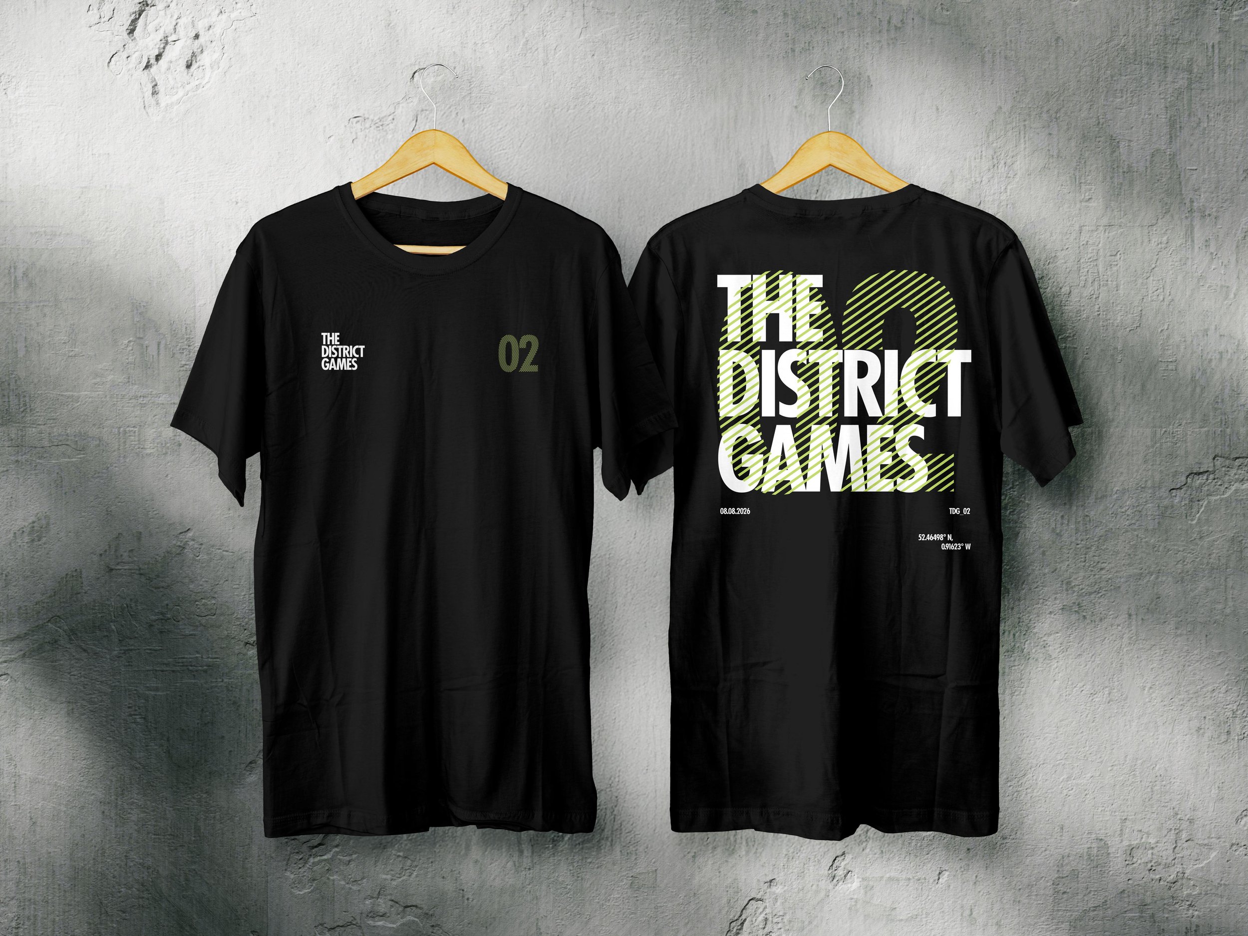 Two black T-shirts hanging on wooden hangers on a concrete wall, one with the text "THE DISTRICT GAMES" and the other with a large stylized graphic and the same text.