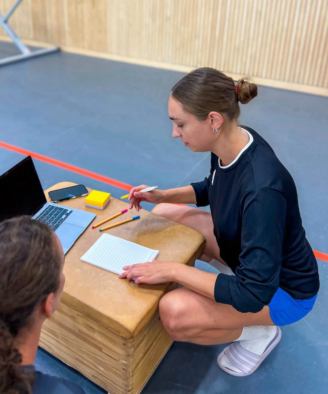In the photo, sports psychologist Eva Sippel is working with an athlete in a sports hall. She is crouching next to a box, which she is using as a table for a laptop, a notepad and pens. Both appear to be concentrating.