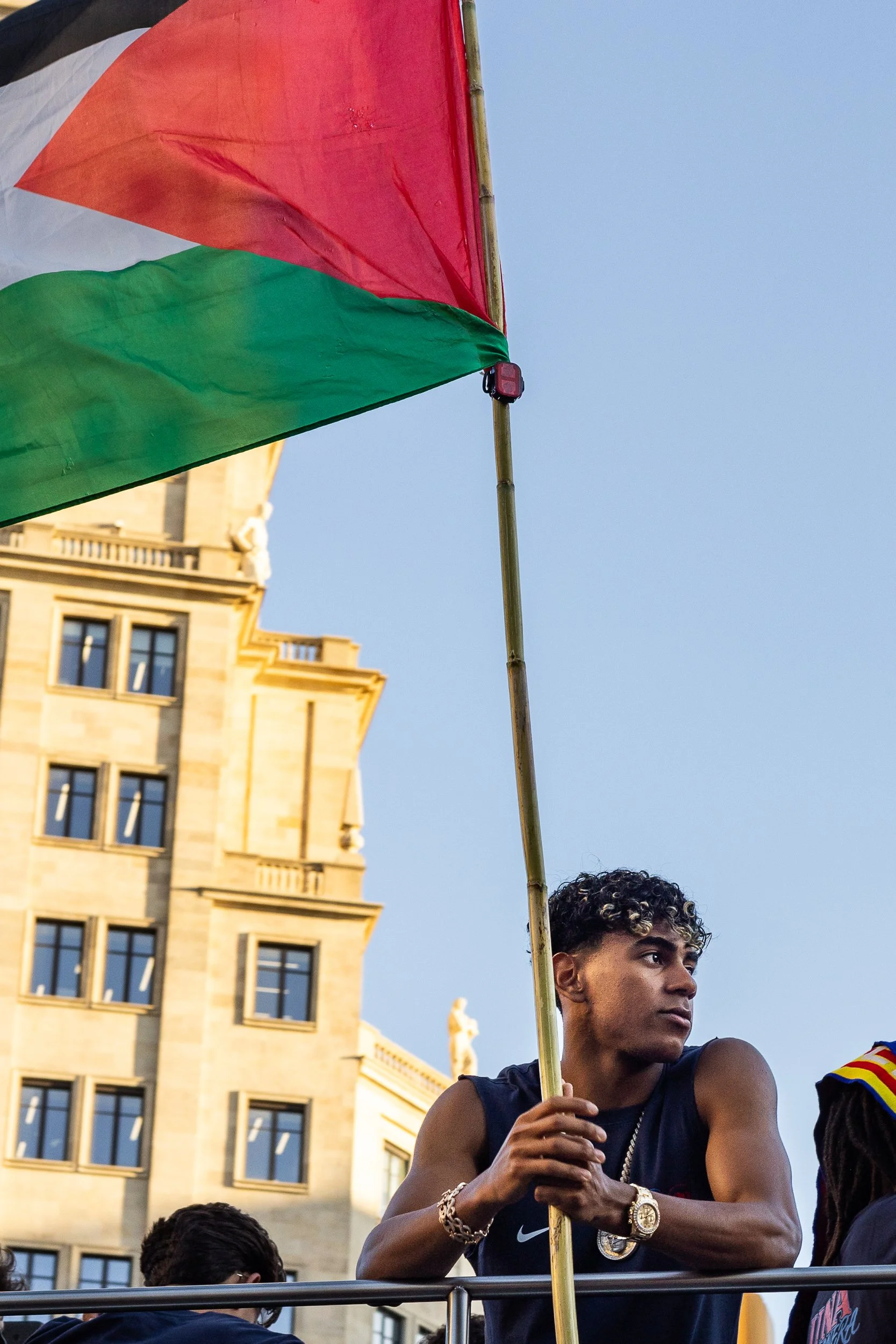 Gold chain, gold watch, and a flag held higher than either. — Barcelona, Spain. 2026