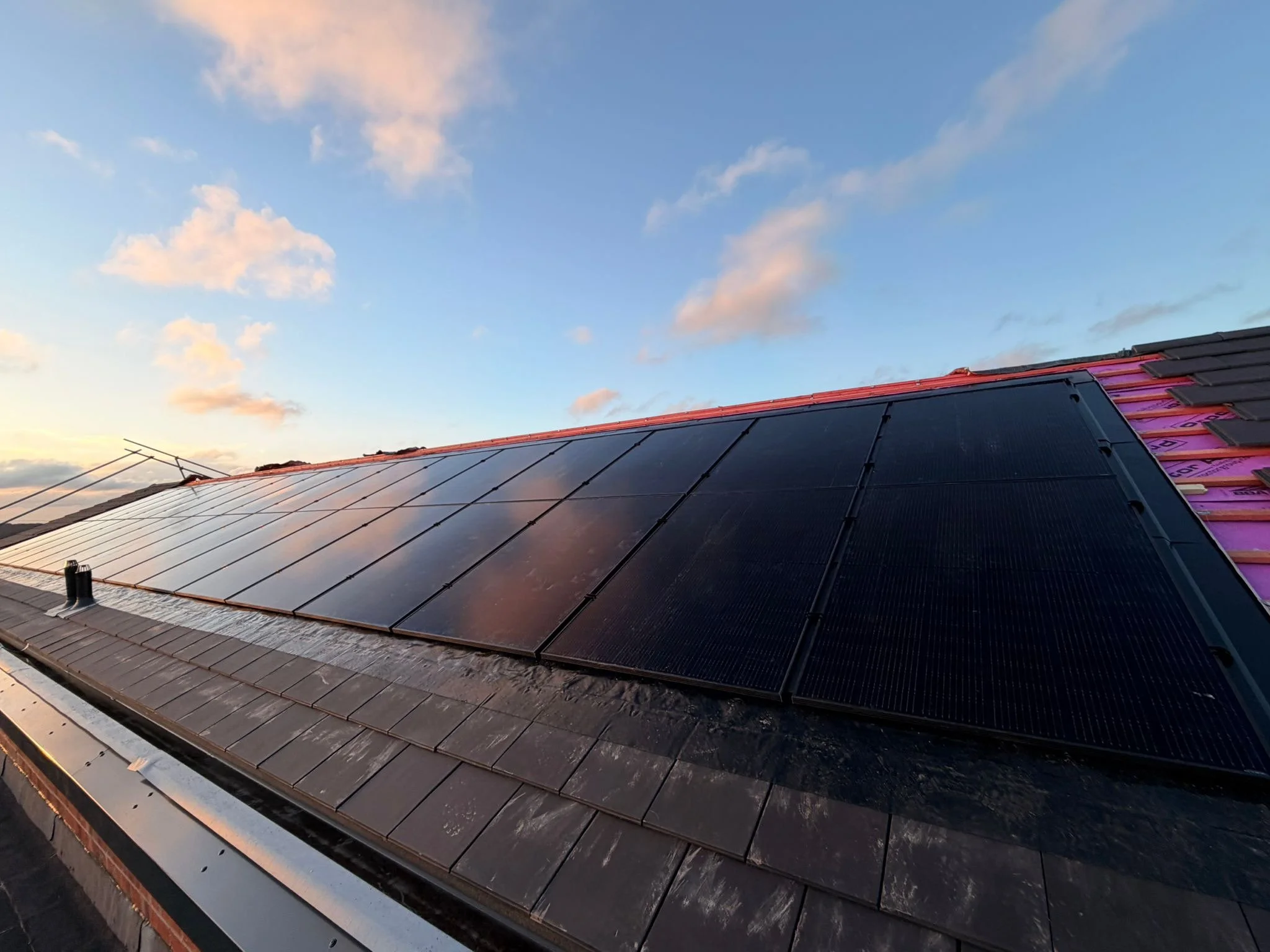Solar panels installed on a roof, with a sunset sky and scattered clouds in the background.