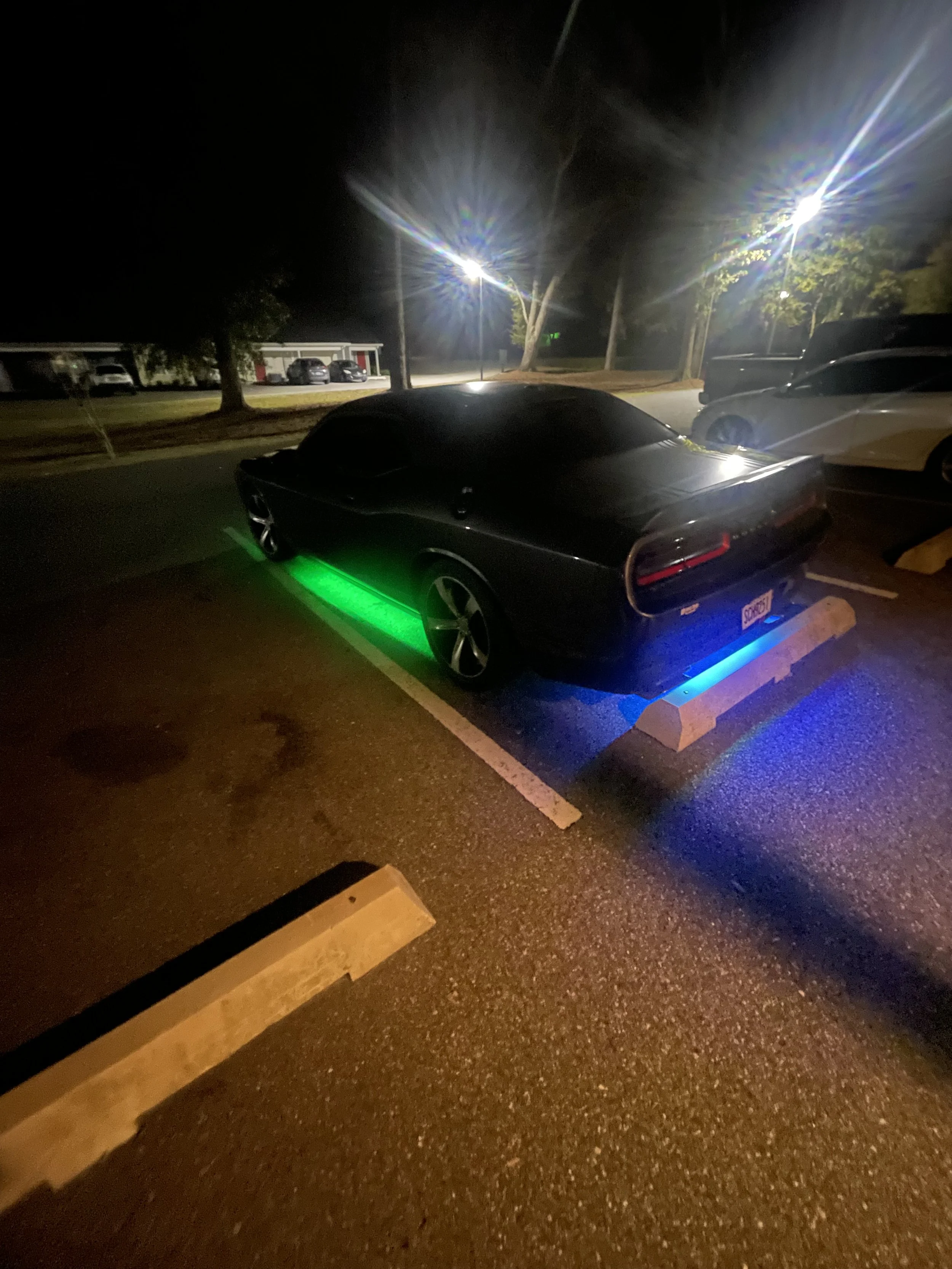 Nighttime parking lot with cars, illuminated by streetlights, with rainbow lens flare effects.