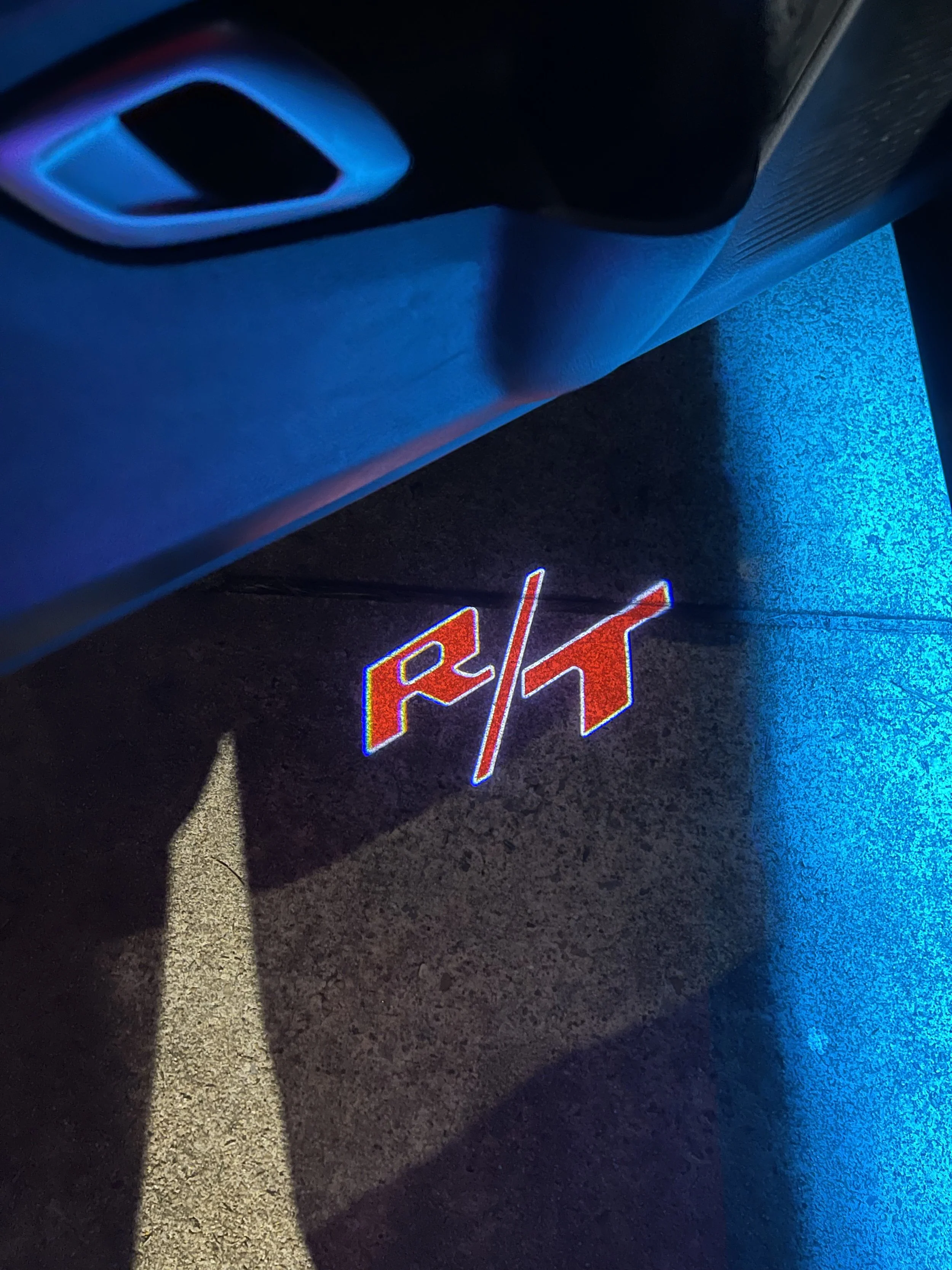 Close-up of a parking lot with a white directional arrow painted on the asphalt, illuminated by blue and red neon lights, with a section of a shoe visible on the left side.
