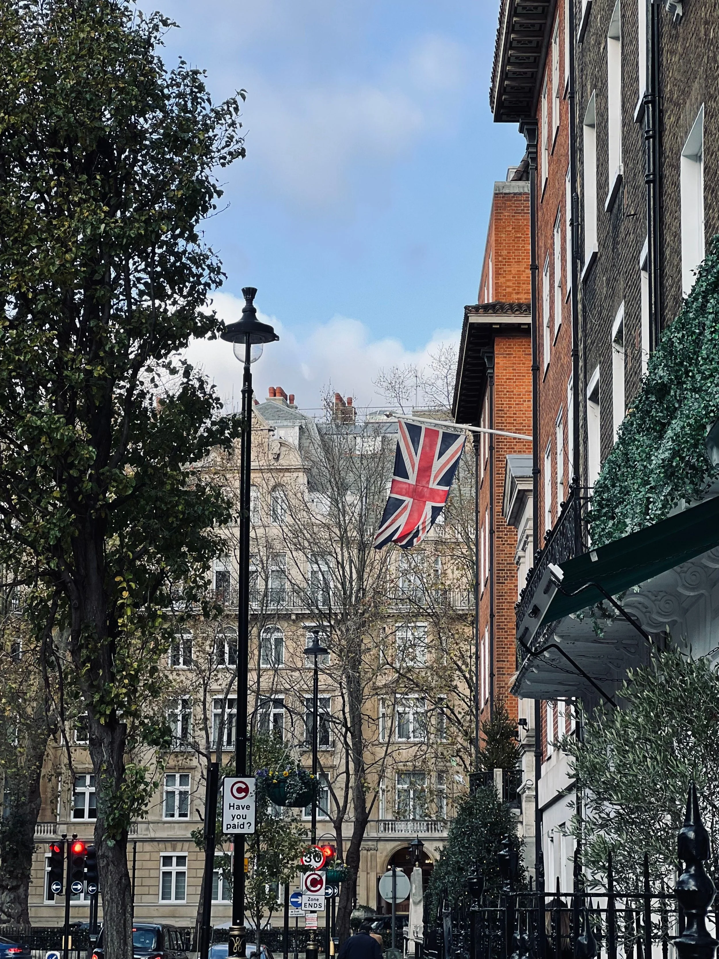 Street scene with buildings, trees, streetlights, Union Jack flag, cars, and various street signs, including a question about parking fees.