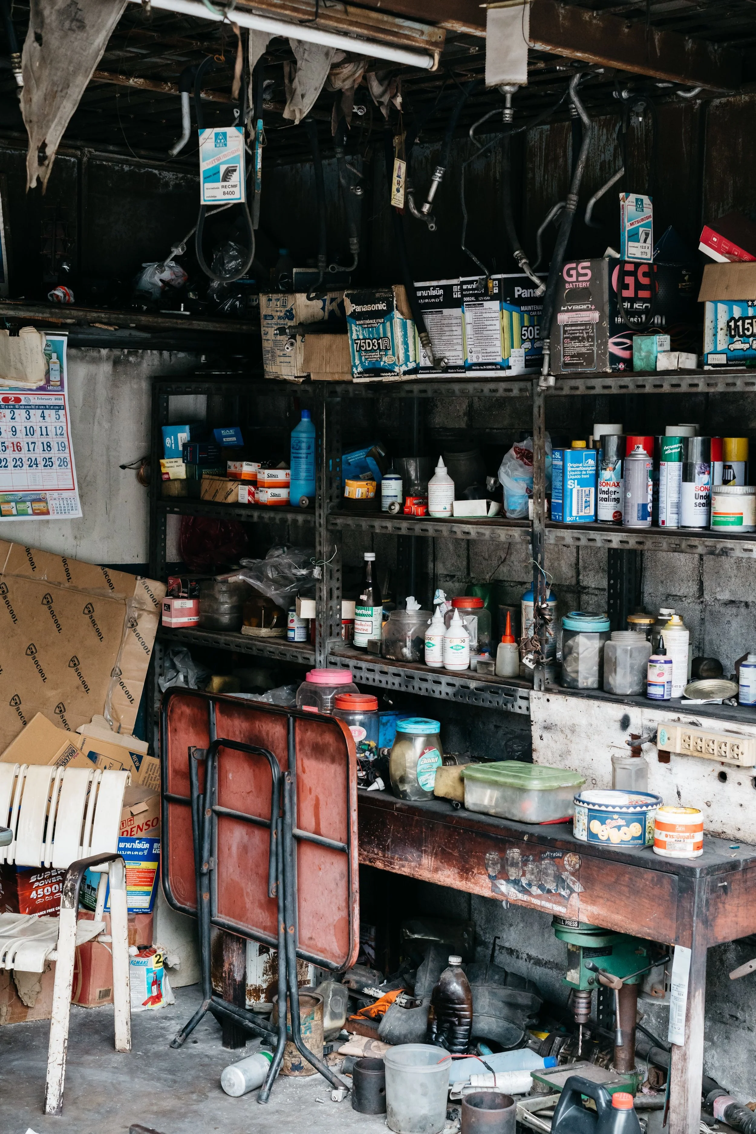 A cluttered workshop with metal shelves filled with car parts, tools, and various containers.