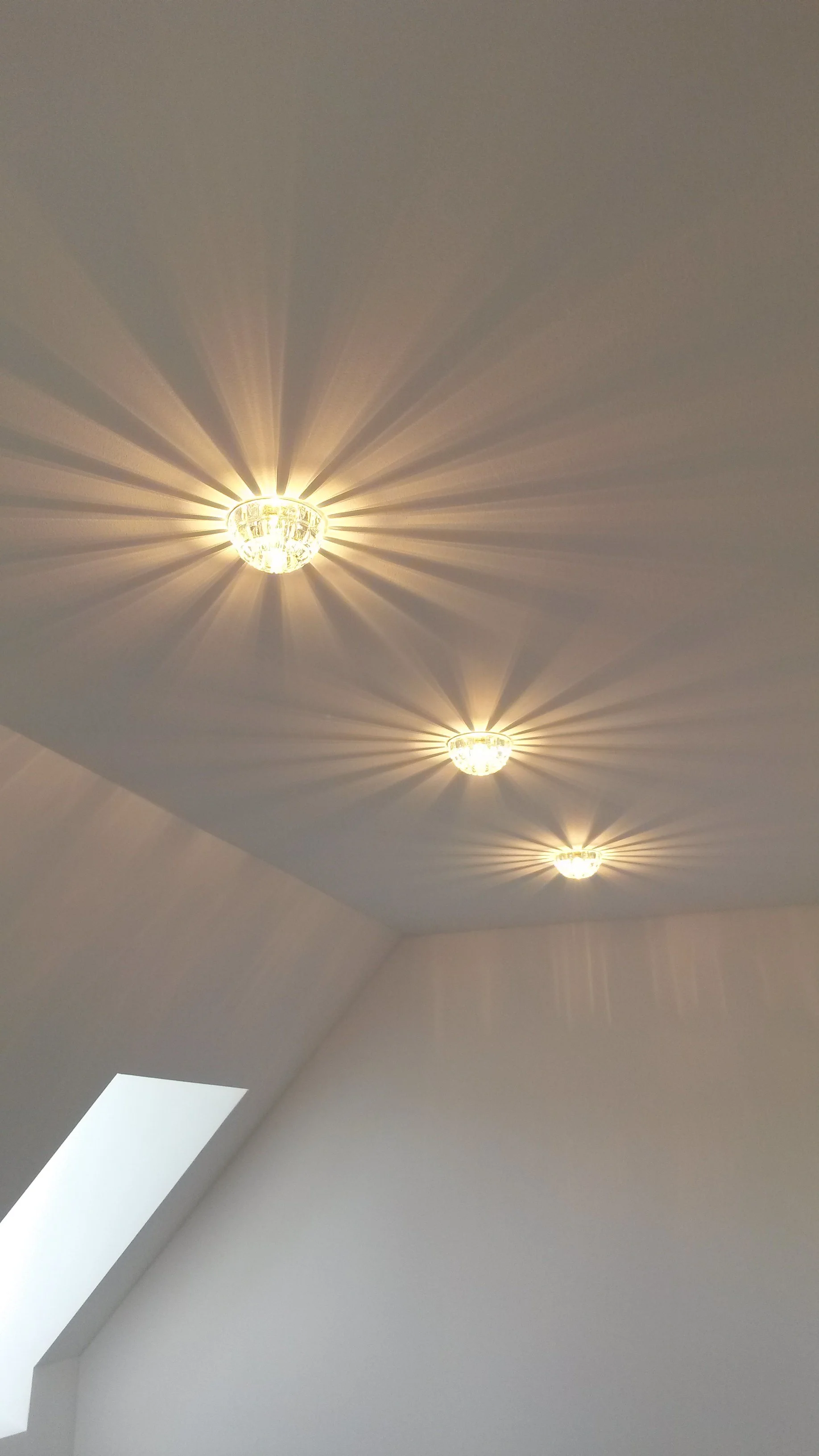 Drei Deckenleuchten mit Kristallkugeln, die Lichtstrahlen an die Decke und Wände werfen.
