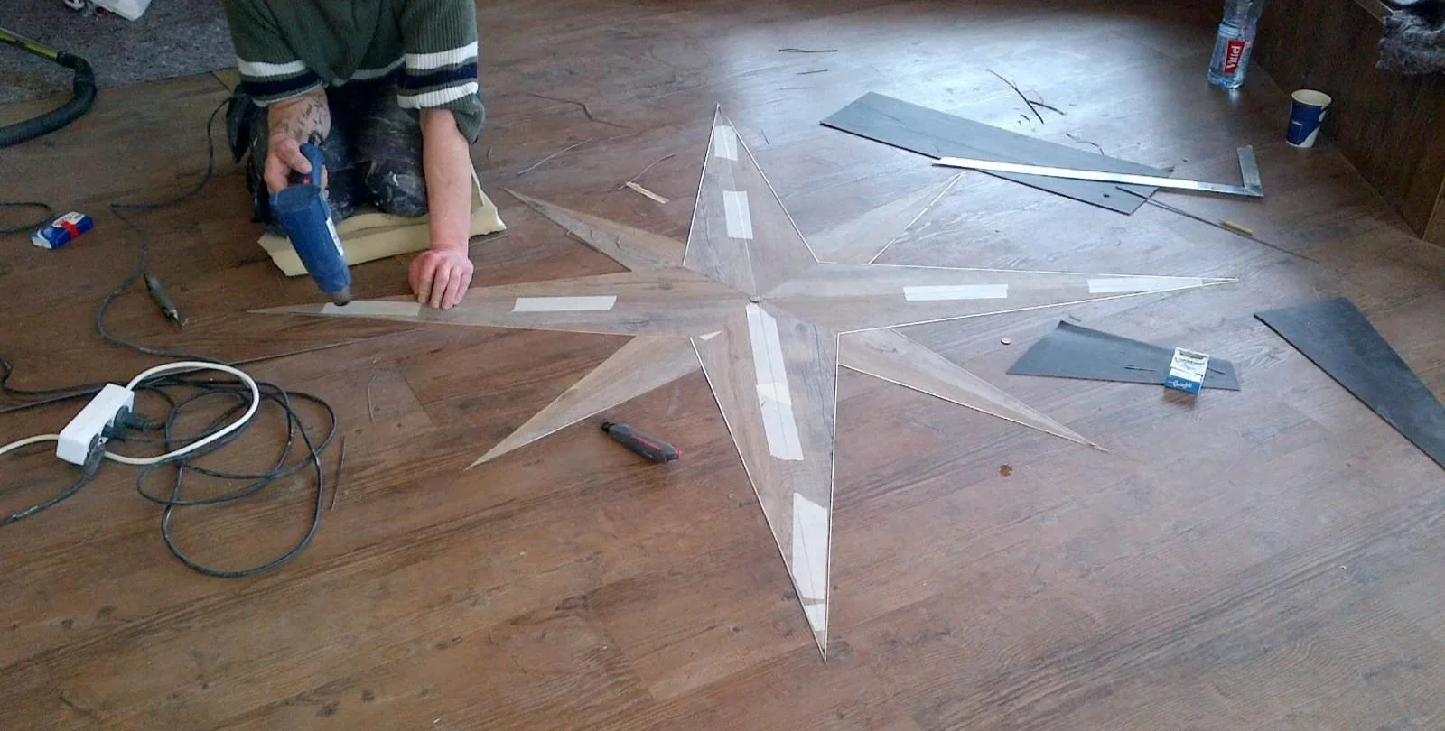 Person arbeitet an einer transparenten Stern-Dekoration auf einem Holztisch, umgeben von Werkzeugen, Kabeln und Bastelmaterialien.