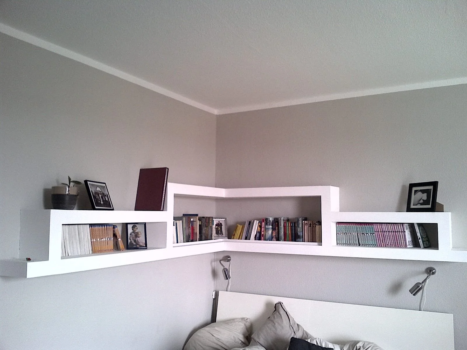 Ein weißer Wandregal mit Büchern, Fotos und Dekorationsgegenständen in einem Schlafzimmer.