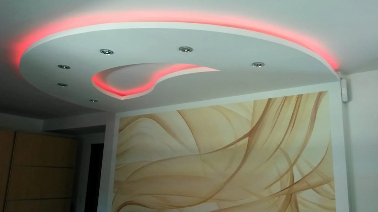 Moderne Deckenbeleuchtung mit roten LED-Lichtern und weißen Deckenplatten in einem Raum mit Wanddekoration.