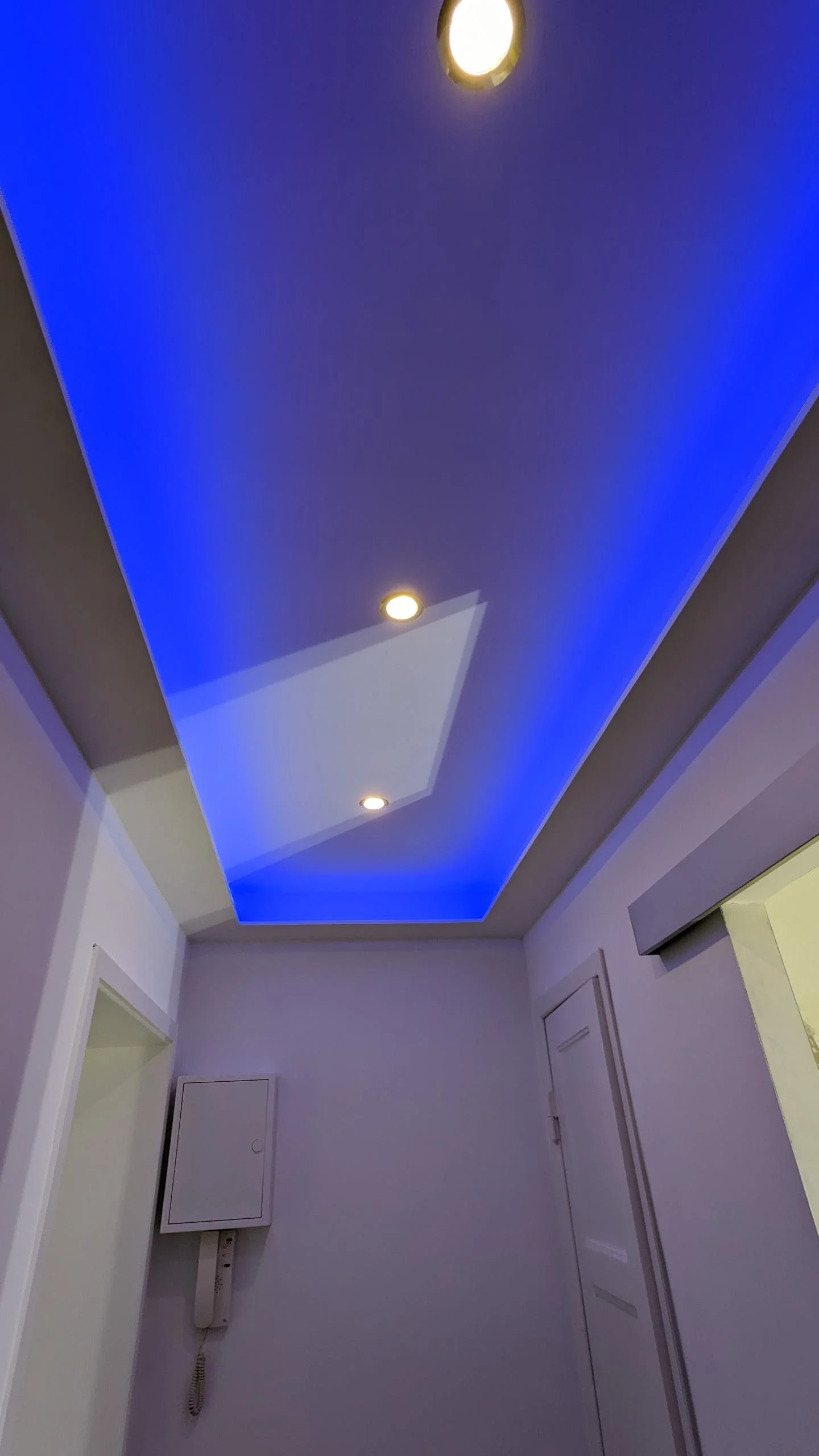 Blick nach oben auf eine Decke mit blauer Beleuchtung und eingebauten Spots im Flur eines Hauses.