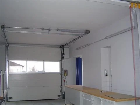 Blick in eine leere Garage mit weißen Wänden, einem roll-up Garagentor, einem Arbeitstisch und einigen Werkzeugen an der Wand.