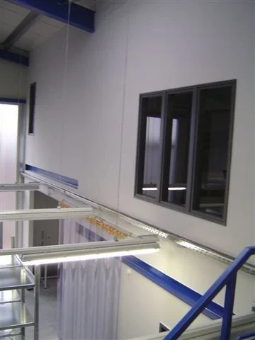 Innenansicht eines modernen Fabrik- oder Lagergebäudes mit Edelstahlregalen und großen Fenstern.