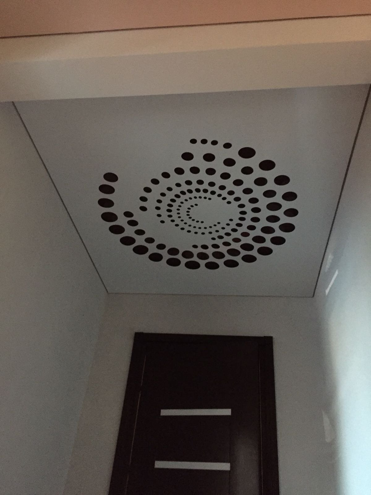 Decke mit runden Lochmustern in Spiralform, vermutlich eine Lüftungsabdeckung in einem Innenraum.
