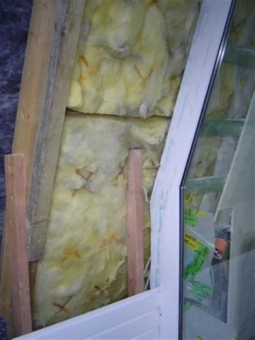 Ansicht einer Wand mit Isolierung, Holzrahmen und einem Fenster in einem Bau- oder Renovierungsbereich.