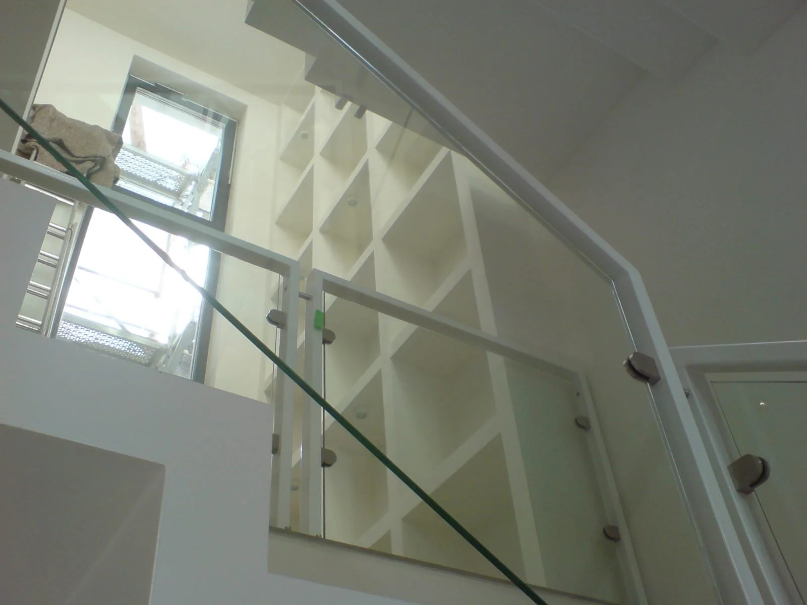 Innenansicht eines neuen Gebäudes mit weißen Wänden, einer Treppe, einem Glaskörpergeländer und einer großen Fensterfront, durch die Tageslicht einfällt.