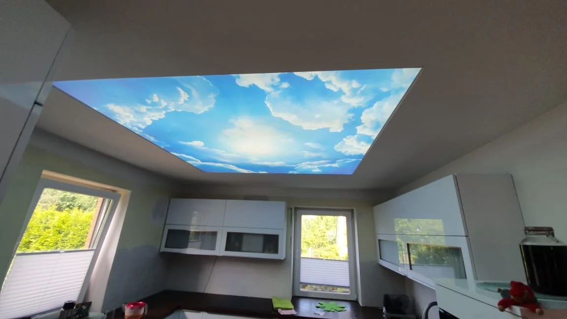 Deckenbeleuchtung mit Himmelsszene, zwei Fenster mit grüner Natur draußen, moderner Küchenraum.
