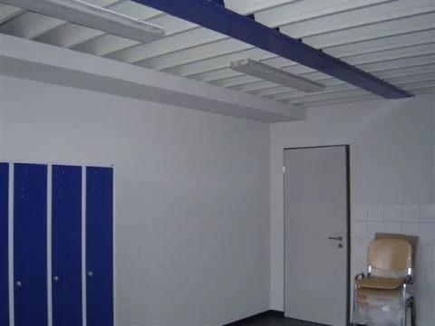 Leerer Raum mit weißen Wänden, blauen Schließfächern, einer weißen Tür und einem Stuhl.