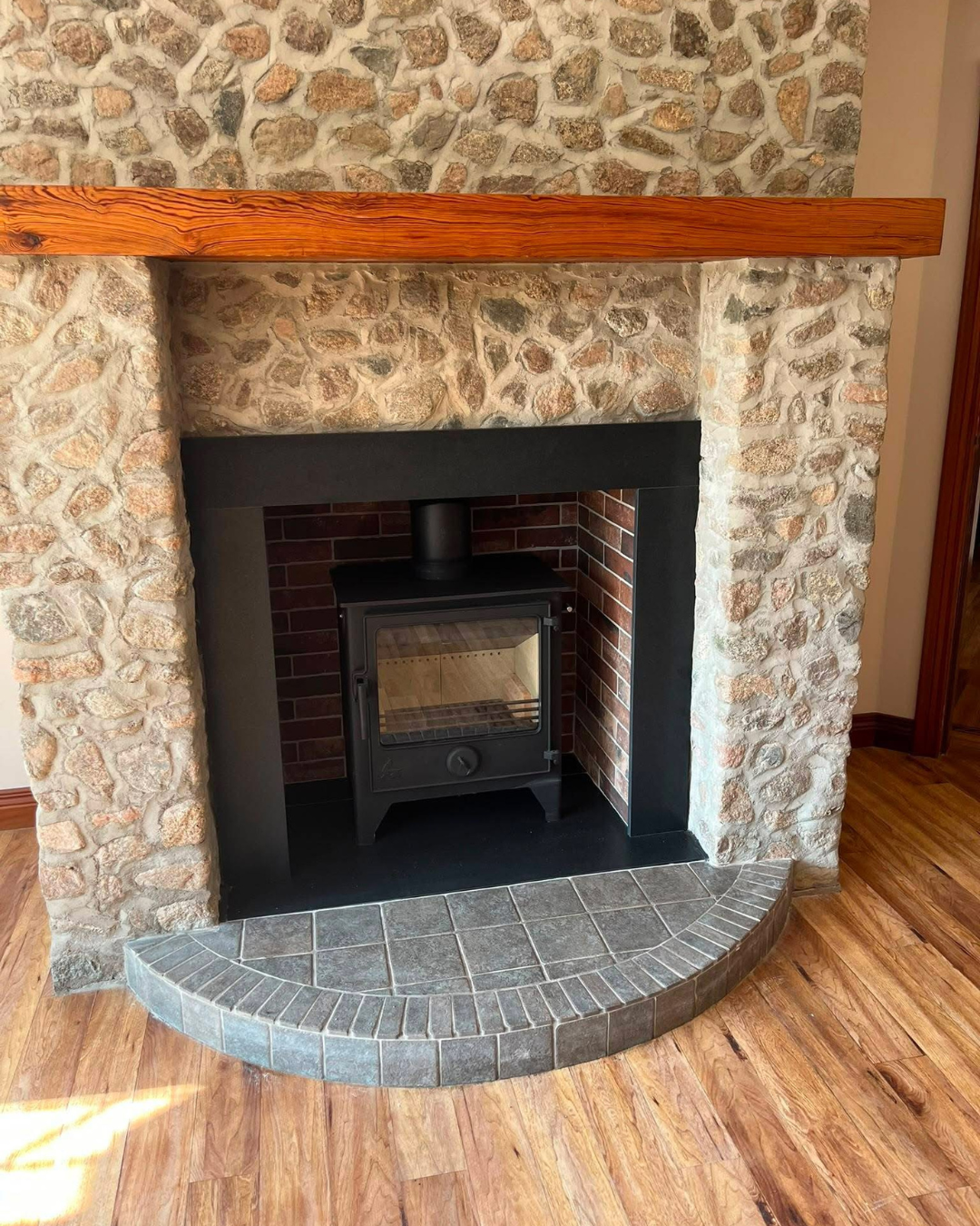 Stone fireplace with a black wood stove, a wooden mantel, and a curved gray tile hearth.