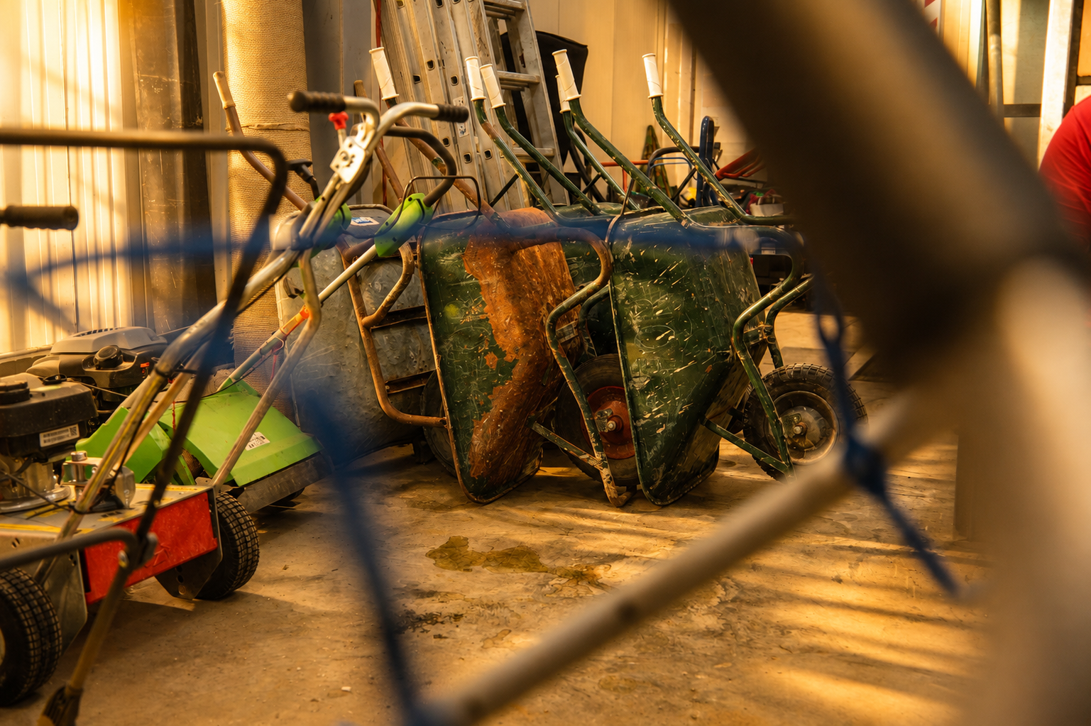 Alte, verrostete springer und Gartenwagen stehen in einem Raum mit Holzbohlenboden, hinter einer blauen Schnur