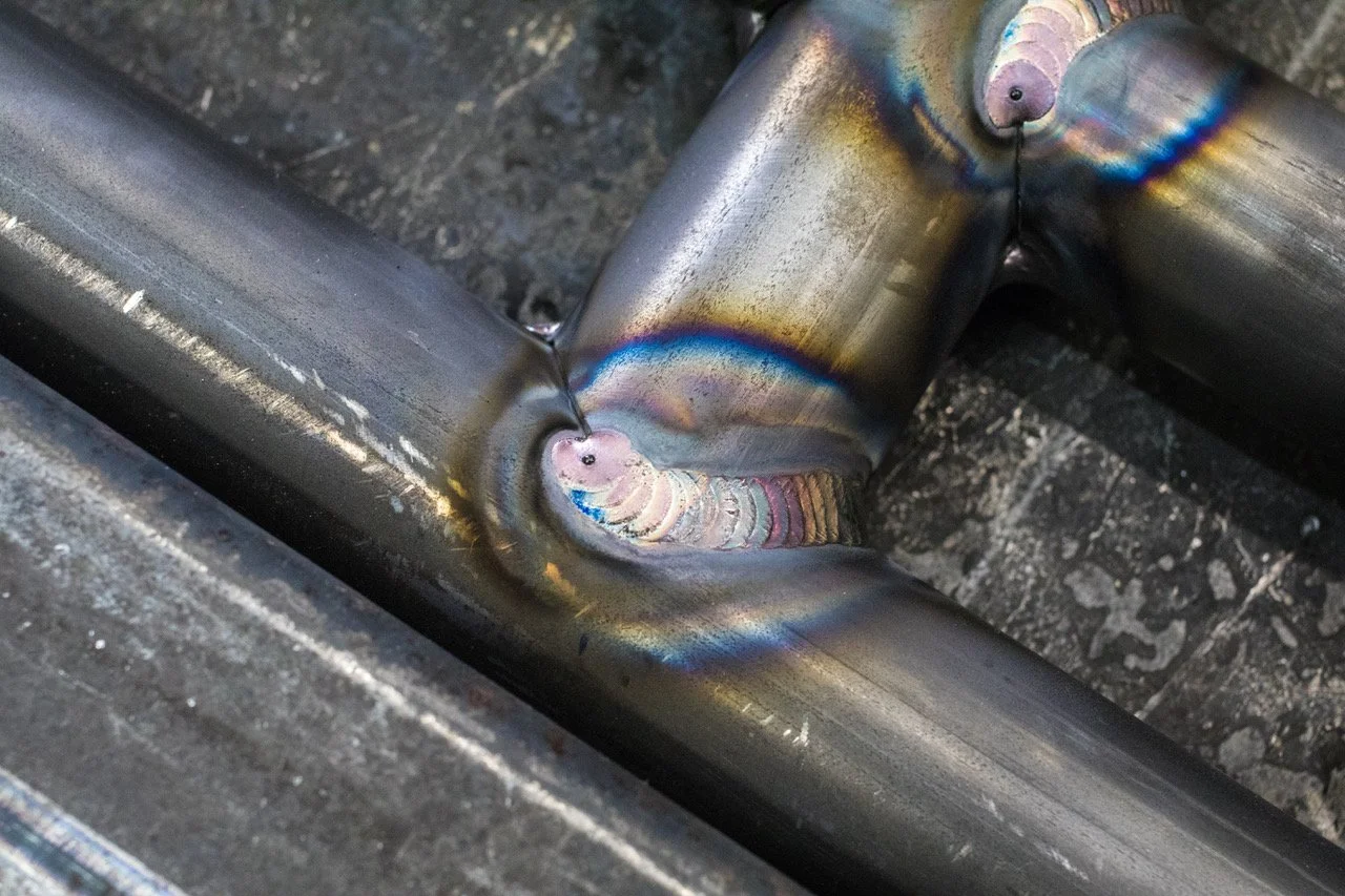 Close-up of a welded metal pipe joint with rainbow-colored heat marks.