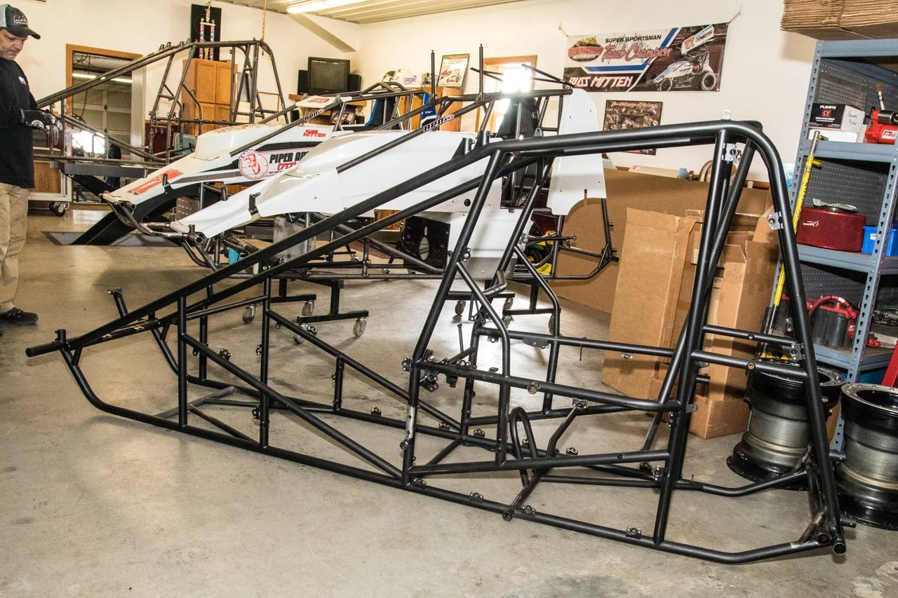 Race car chassis in a workshop with tools and posters on the wall
