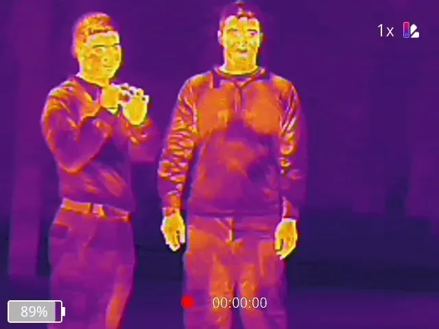 Two people standing side by side, captured in a thermal or infrared image with color variations indicating temperature differences.