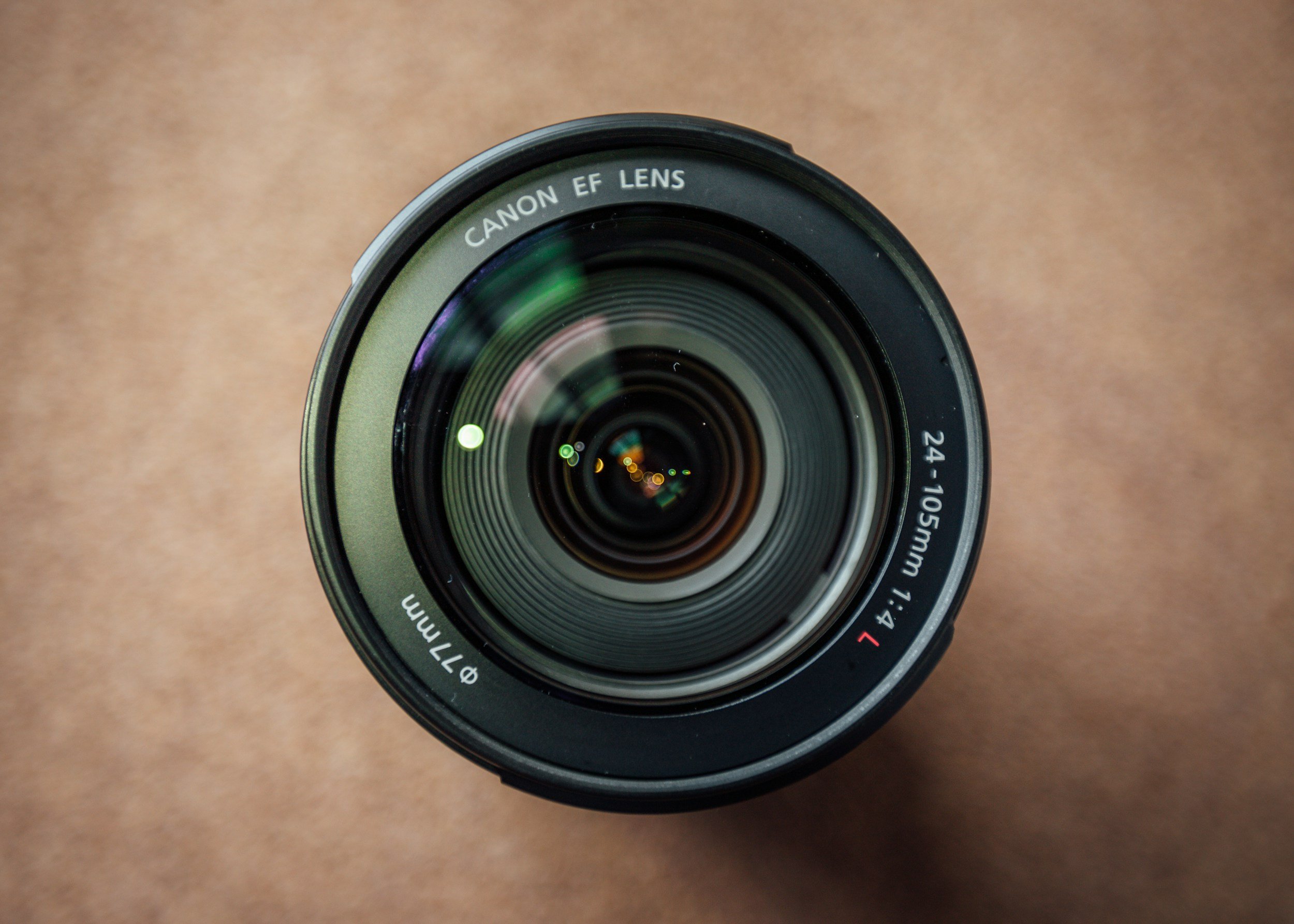 A close-up photo of a Canon EF lens, showing the front element and focus ring, with a plain background.