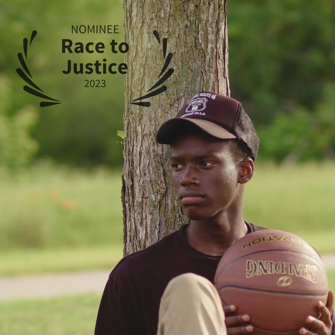 A young man leaning against a tree holding a basketball, wearing a black T-shirt and a brown cap, outdoors with a blurred green background. Text on the image reads 'Nominee Race to Justice 2023'.
