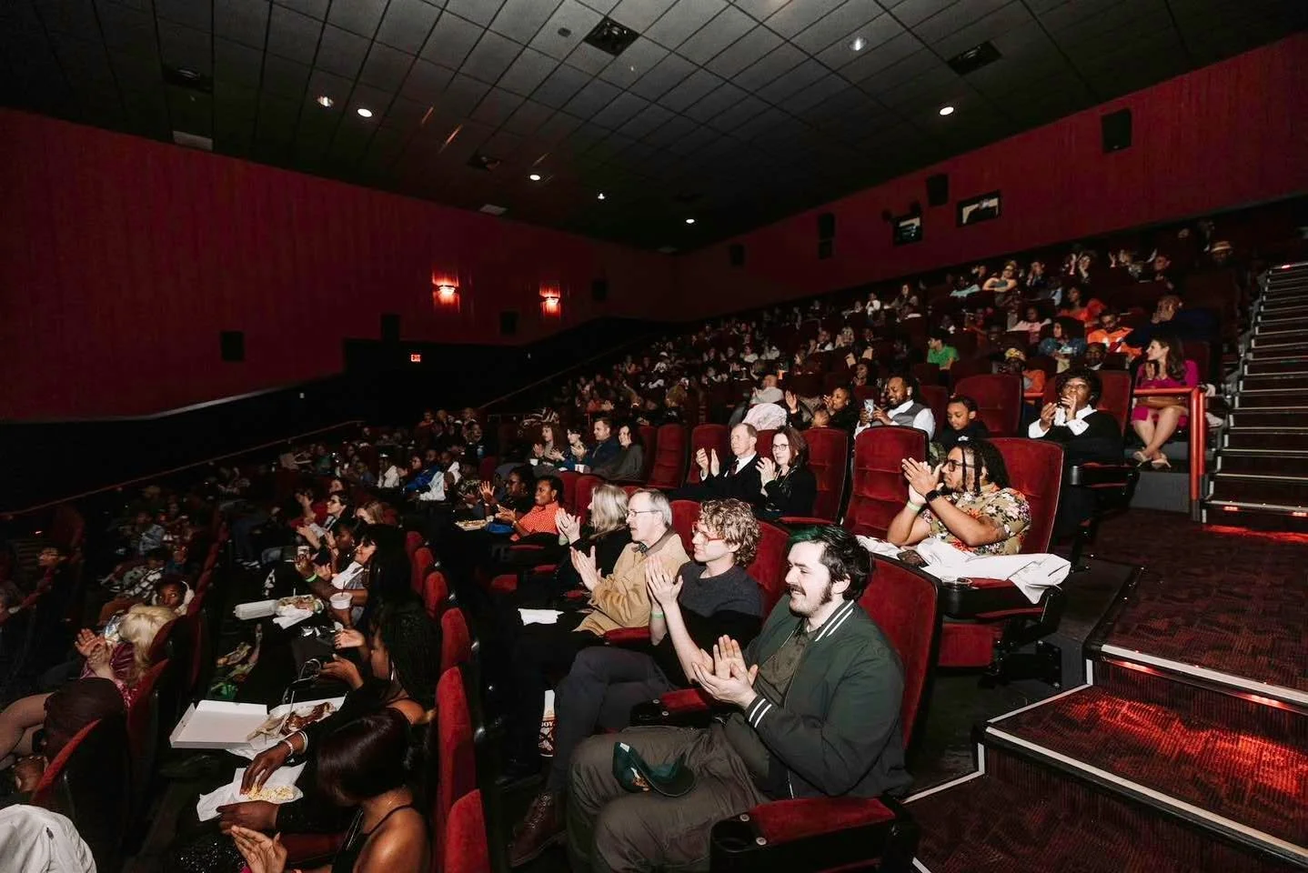 Audience sitting in a theater, clapping and watching a performance or presentation.