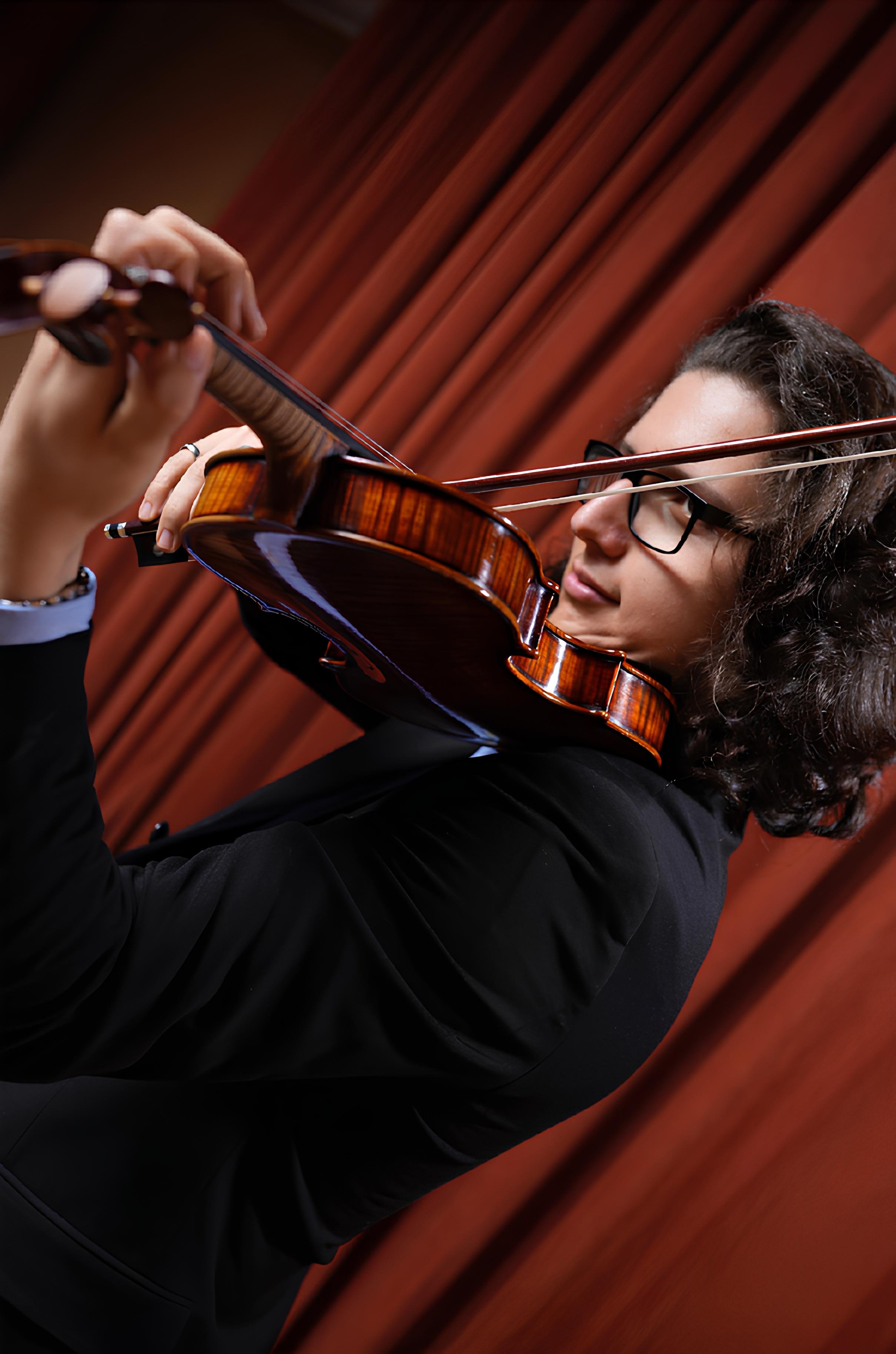 Woman with dark curly hair and glasses playing a violin against a wooden background
