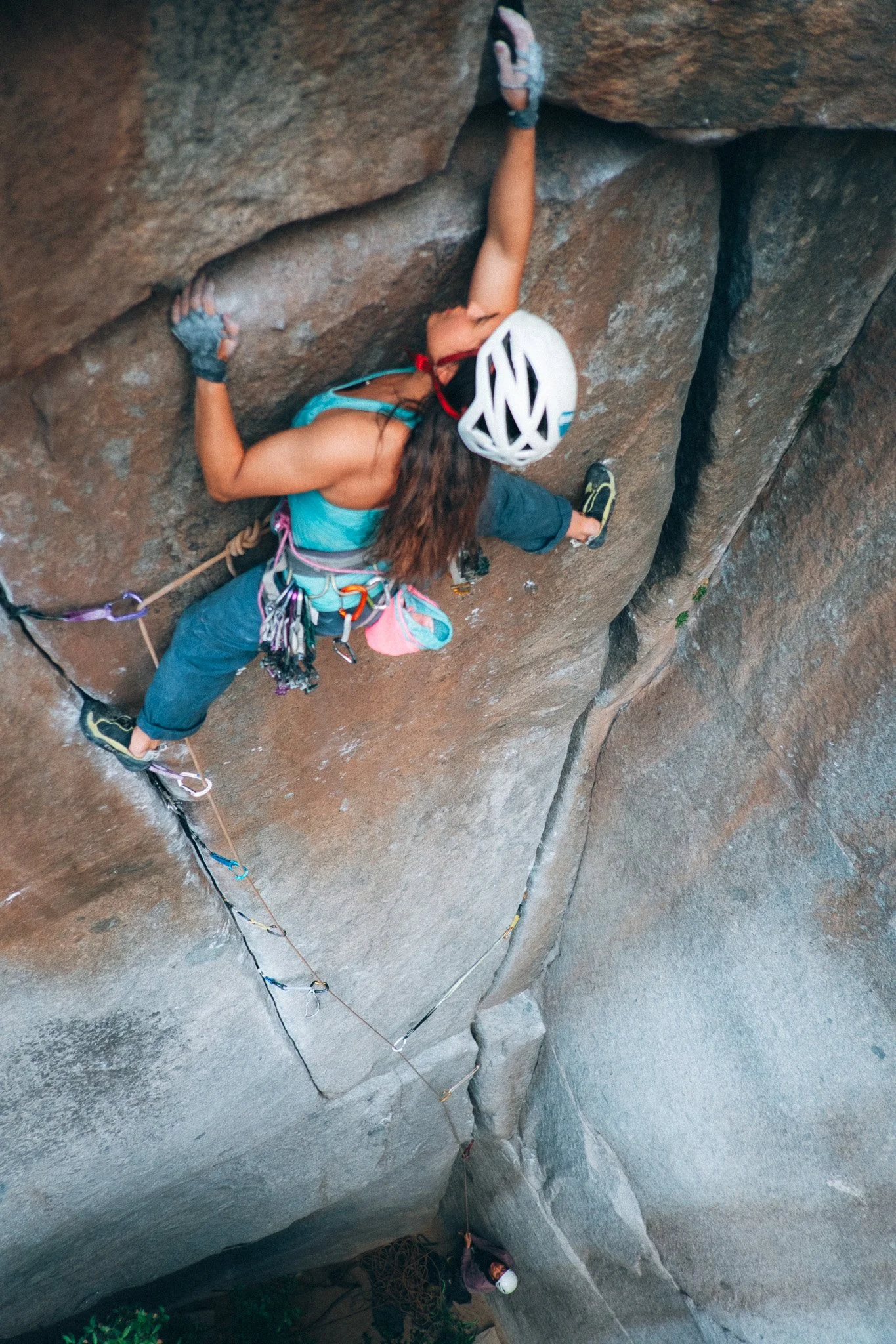 Outdoor Sportfotografie eine Frau welche an einer senkrechten Felswand mit Kletterausrüstung klettert, einschließlich Helm, Klettergurt und Seilen.