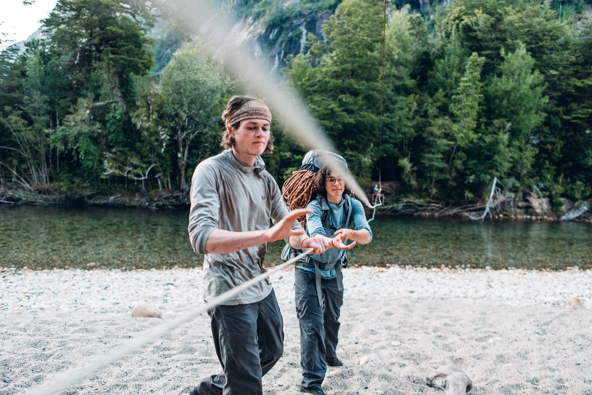 Adventure Photography von zwei Personen an einem Fluss in einer grünen, bewaldeten Berglandschaft in Cochamo Valley.