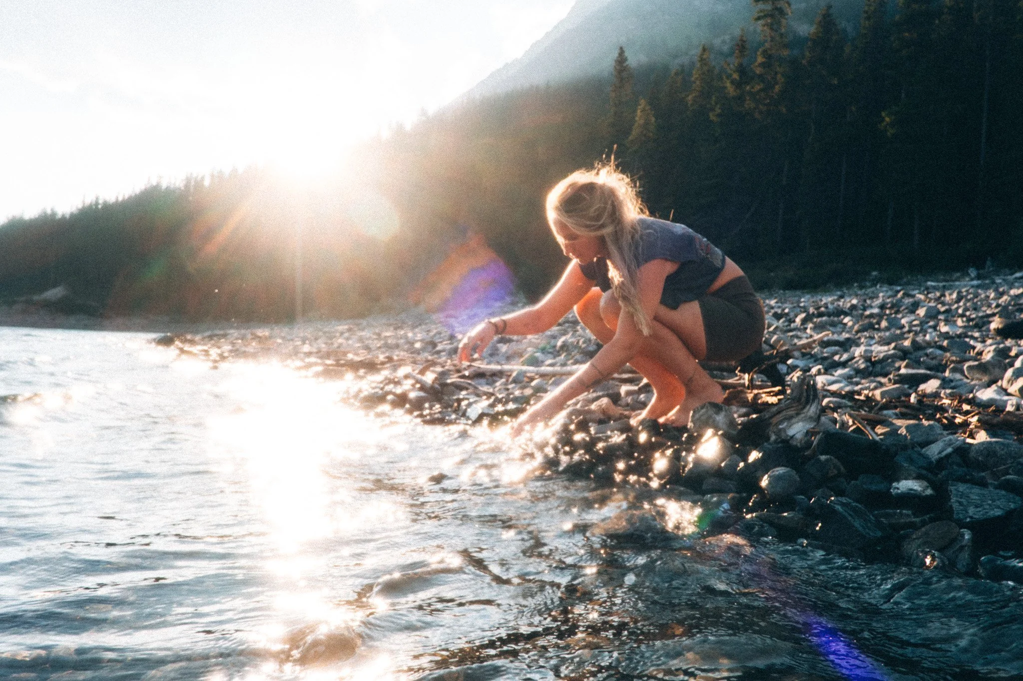 Reise- und Lifestyle Photography eines Mädchens, welches am Ufer eines Flusses sitzt und mit Wasser in natürlichem warmen Licht spielt.