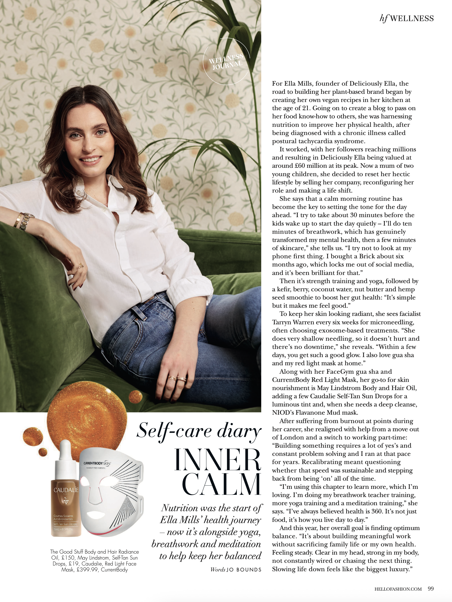 A woman with shoulder-length brown hair and blue eyes, smiling, sitting on a green sofa. She is wearing a white shirt and denim jeans, with her left arm resting on the back of the sofa. The background features a wallpaper with a floral pattern and a tall green plant. There are also some skincare products and an illustrated white facial mask with a red smiley face design at the bottom of the image.