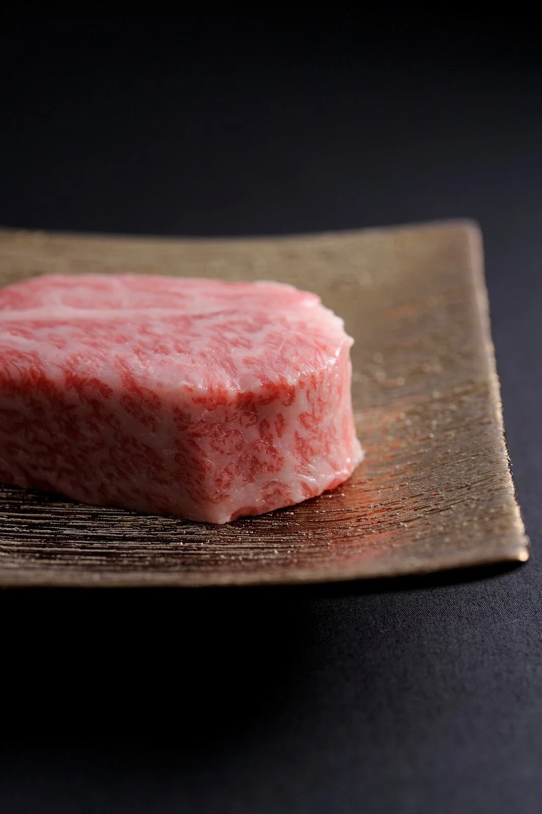 Close-up of raw, marbled wagyu beef steak on a wooden board against a black background.