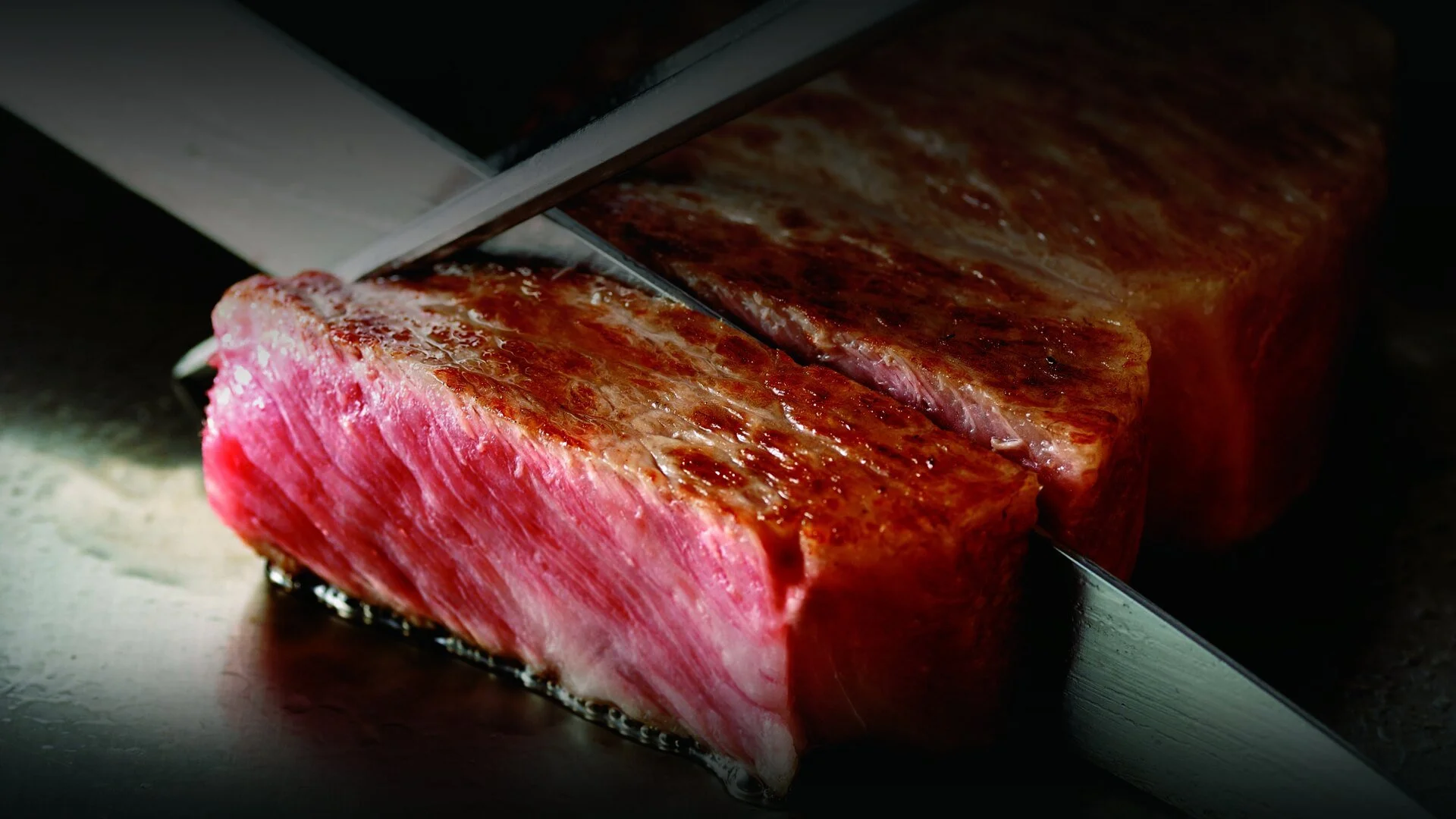 A close-up of a large cut of red meat being sliced with a sharp knife.