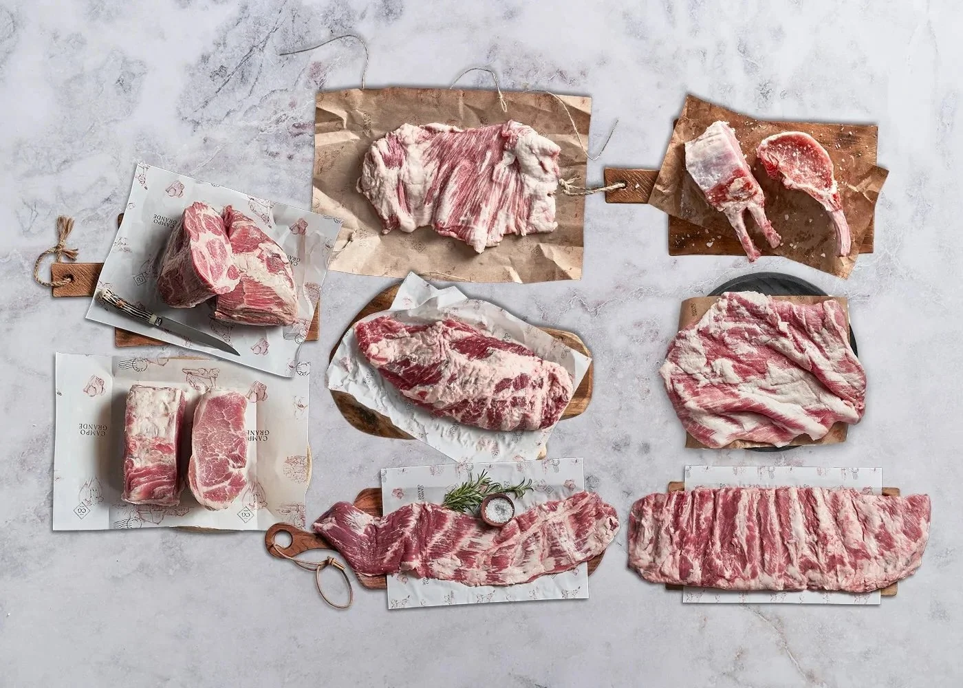 An assortment of raw meats including beef and pork cuts arranged on wooden boards and parchment paper on a marble surface.