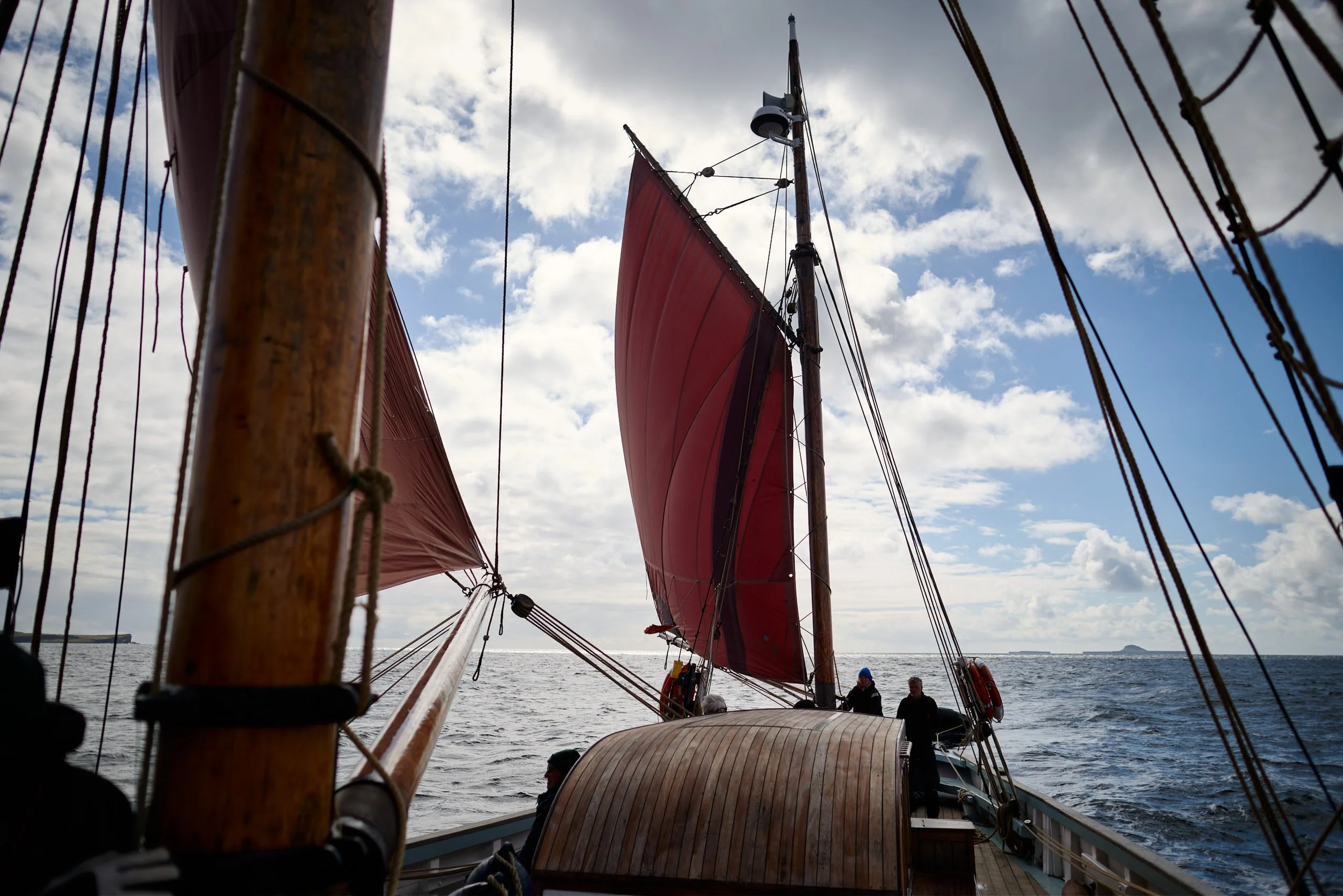 Looking up at a Provident's red sail as it floats on the water with cloudy sky overhead.