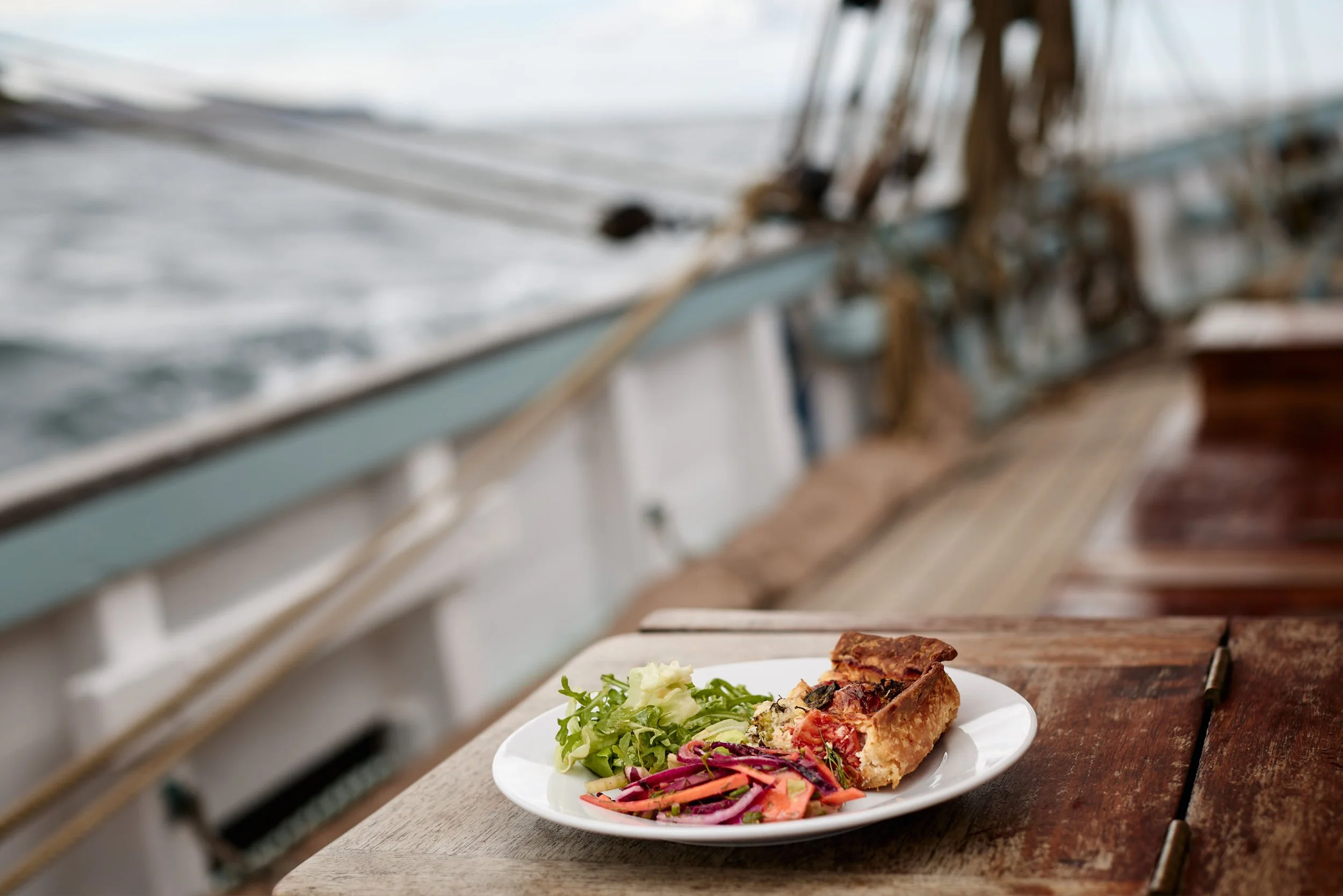 A plate of food with salad and a slice of vegetable quiche or savory tart on a wooden surface, with a kitchen oven in the background.