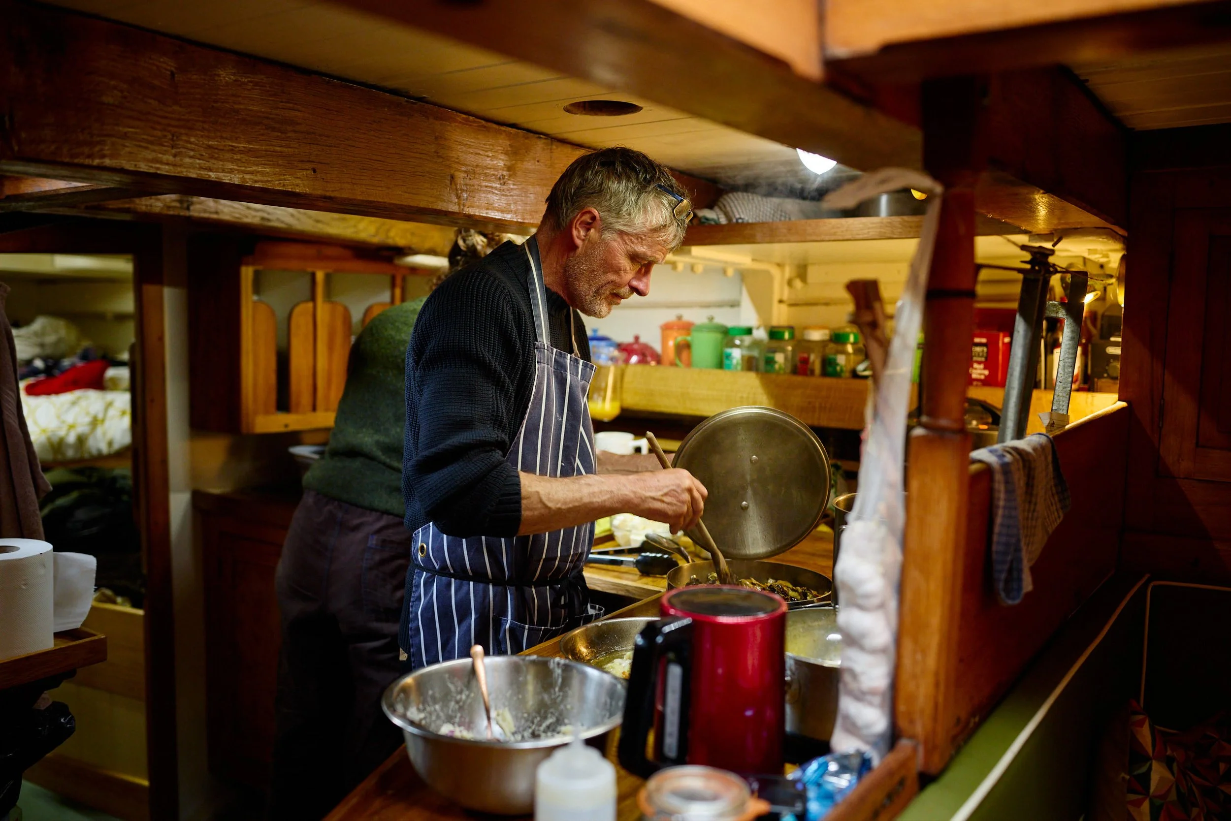A man wearing a striped apron is cooking in a cozy wooden kitchen.