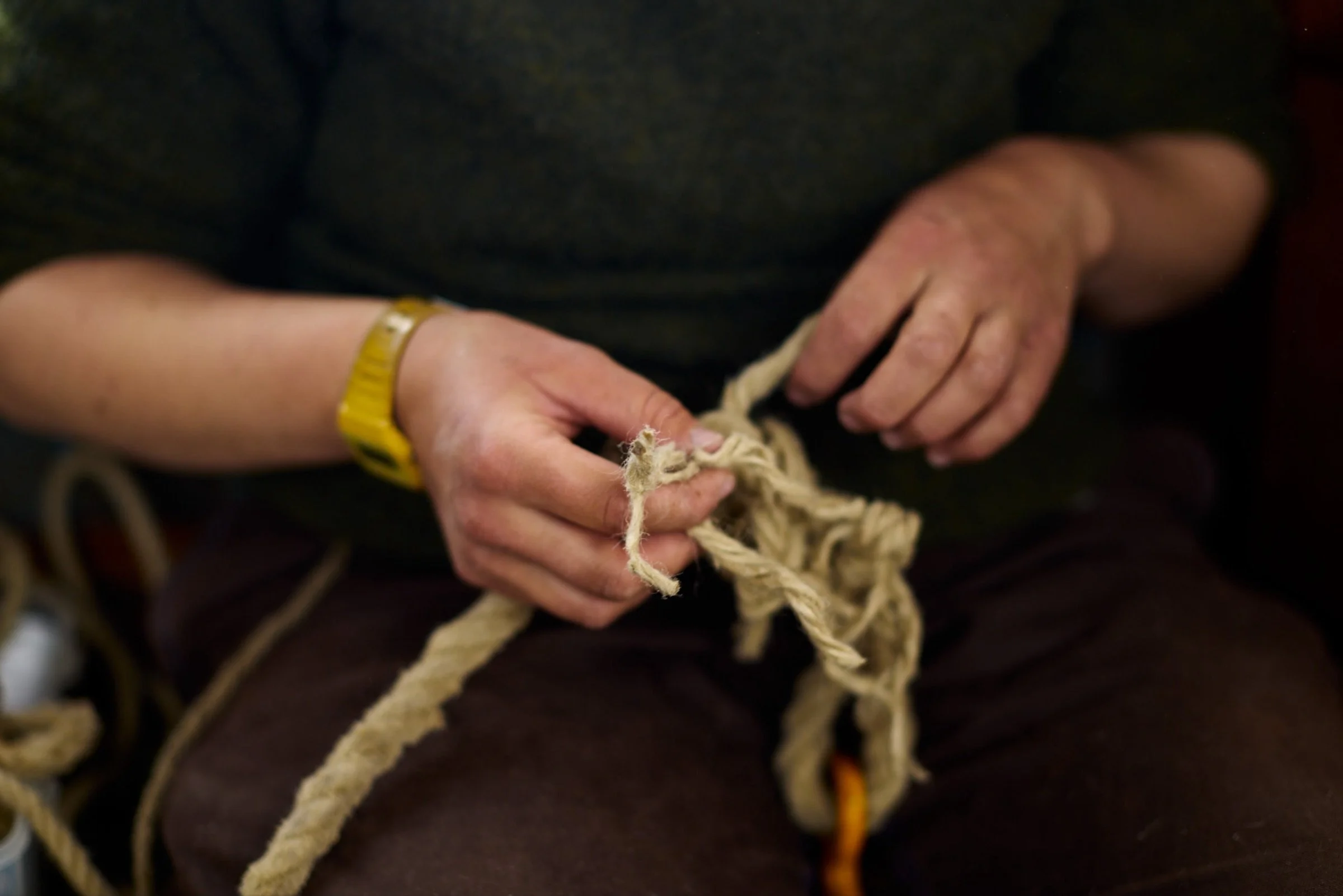 A person is holding a piece of yarn or string with both hands. The person is wearing a black shirt and a yellow wristband on their left wrist.