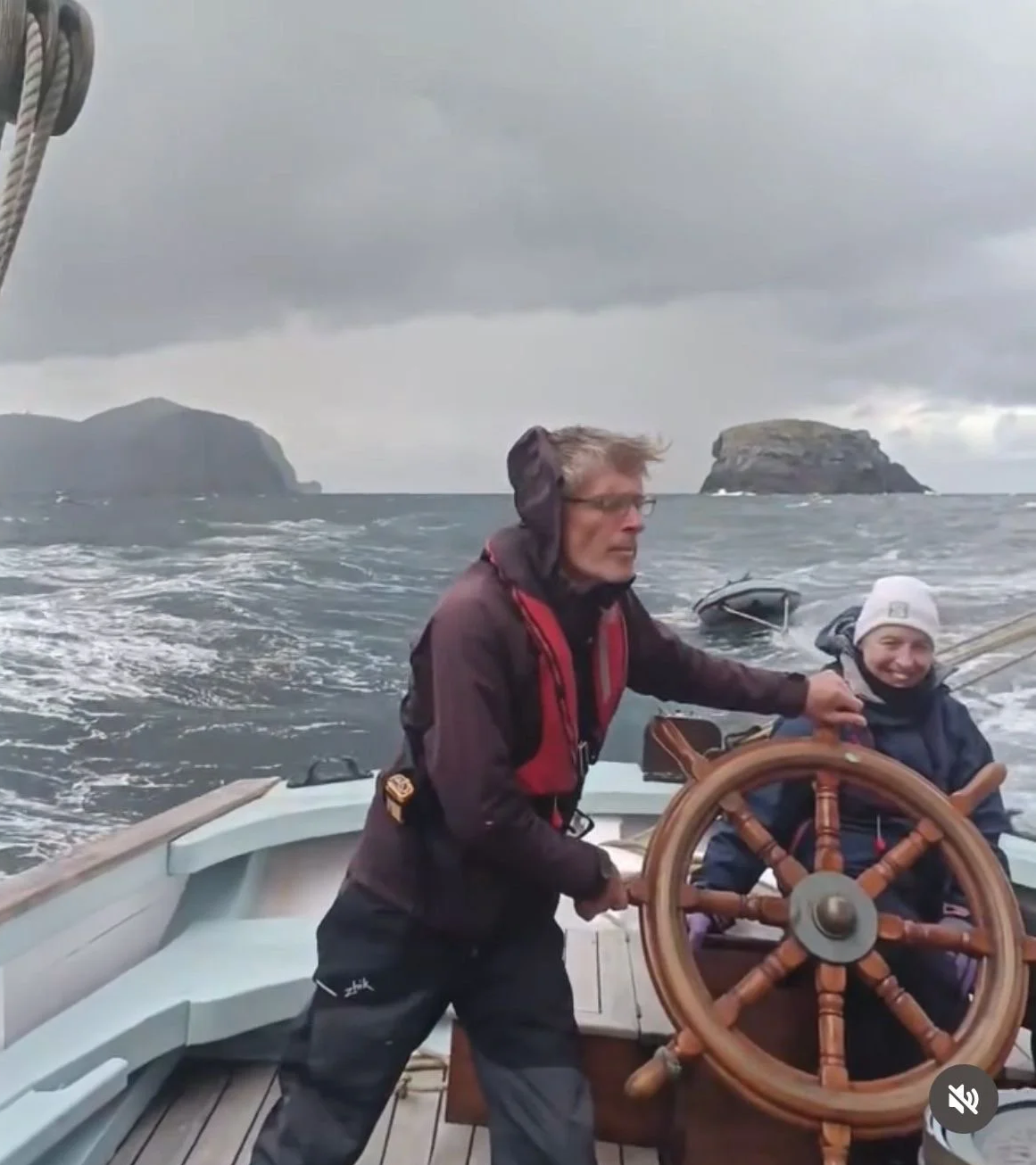 Two people on a boat navigating through choppy waters with islands in the background under cloudy skies.