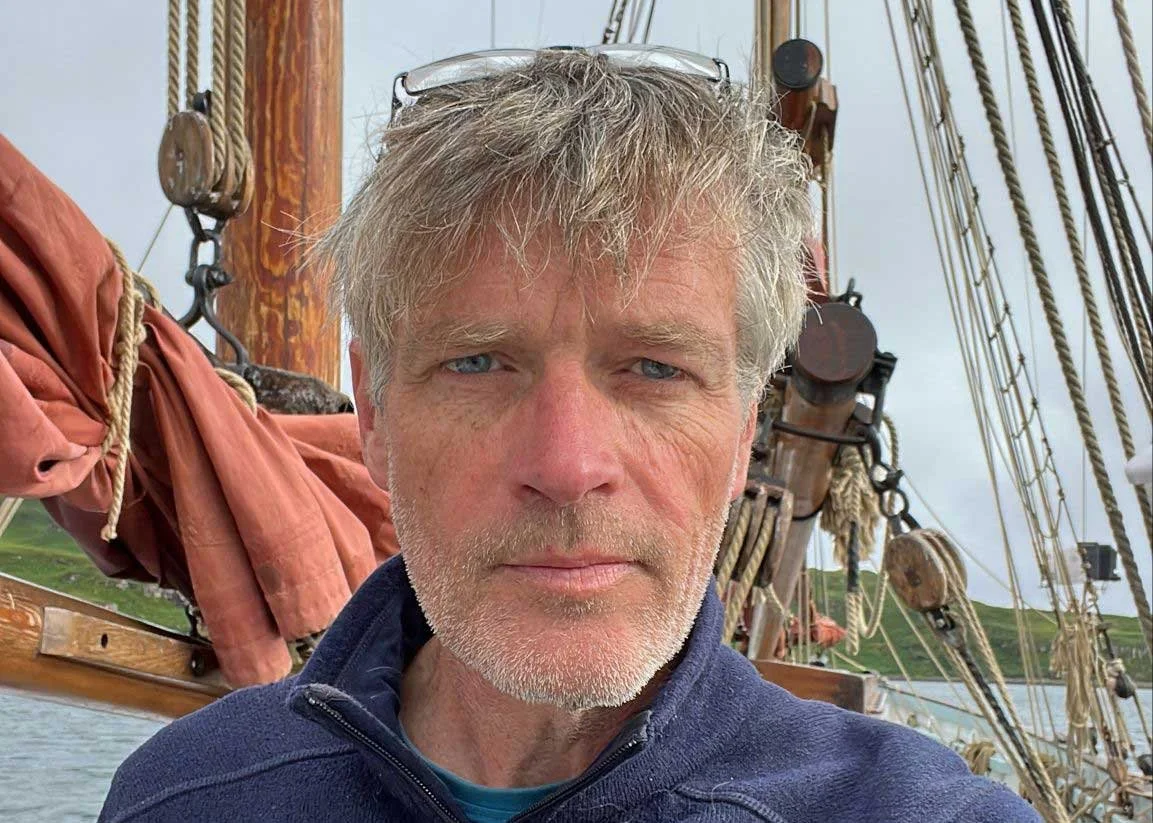 Skipper Steve Jones, with masts and ropes in the background on a cloudy day.